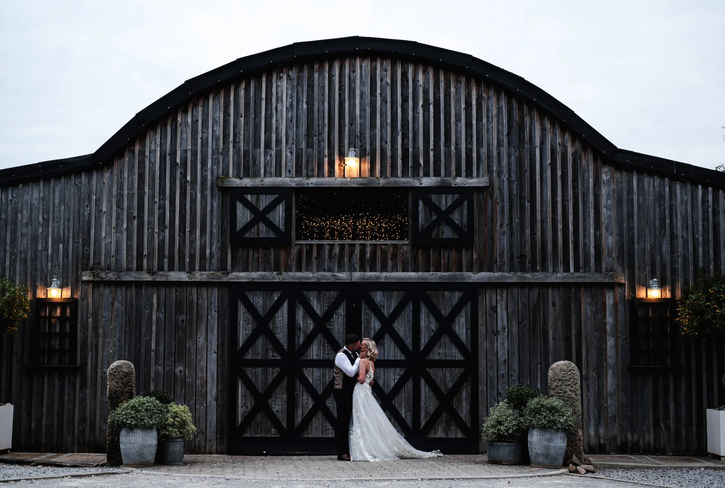 Wedding Photographer Cheshire - Bride and groom facing each other in an embrace in front of a dark wooden barn. 