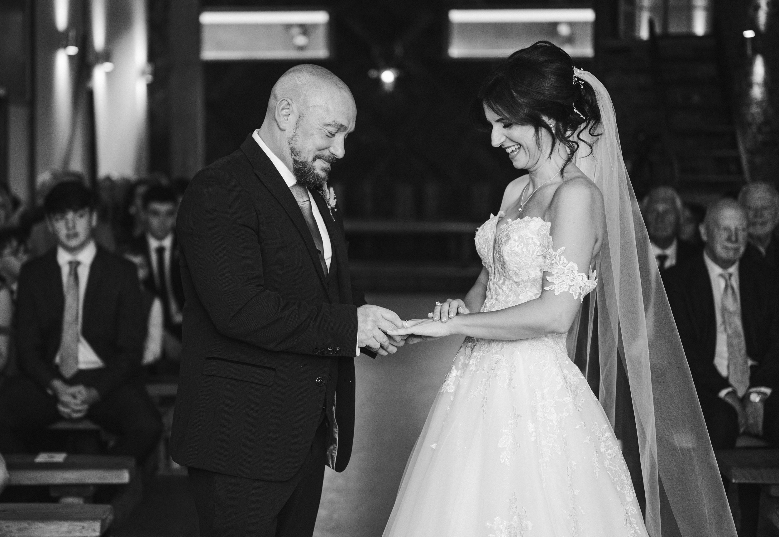 Wedding Photography Cheshire - Black and white image of a bride and groom exchanging rings during a wedding ceremony and laughing