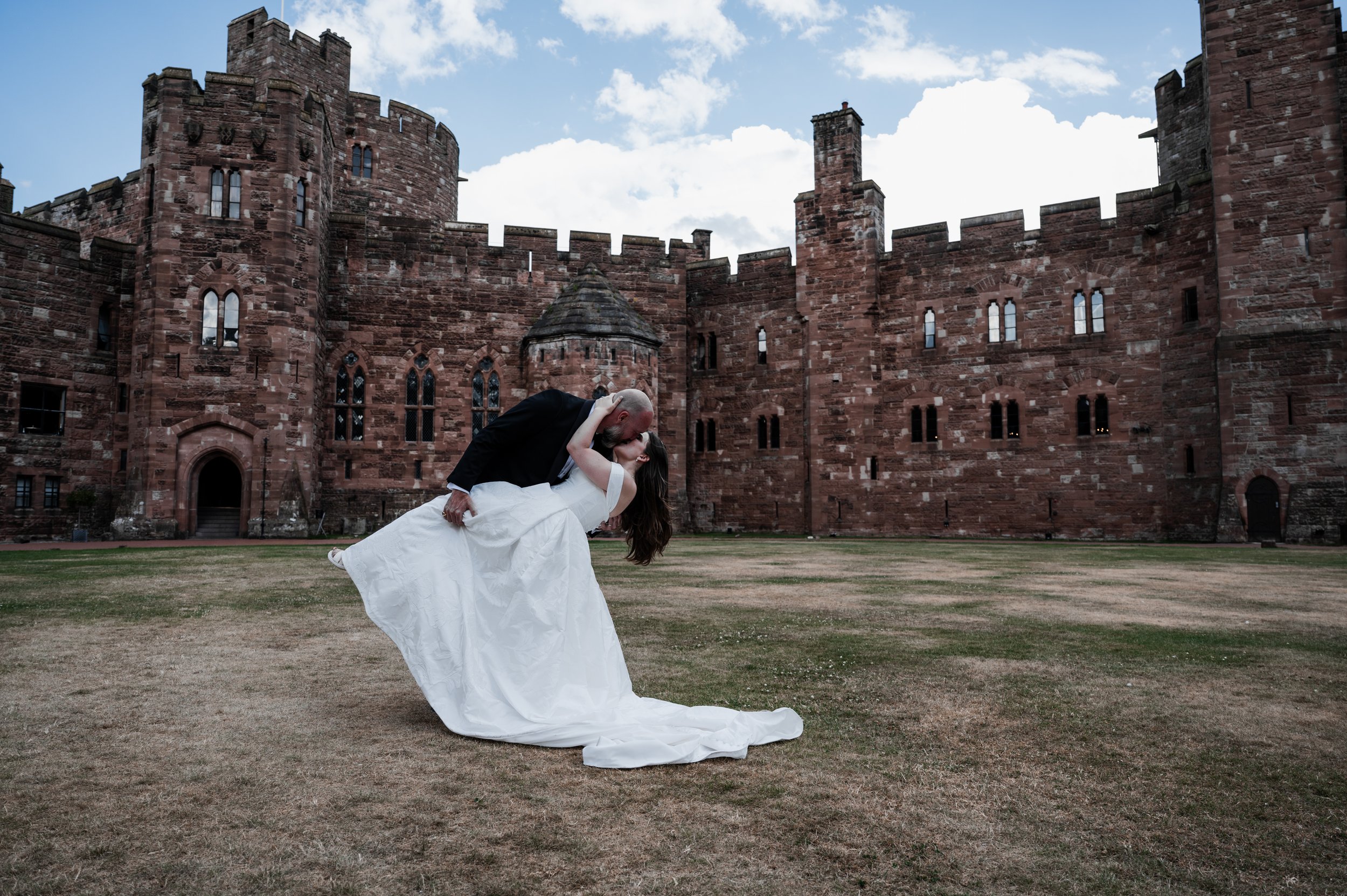 Peckforton Castle - bride being dipped for a kiss from the groom in wedding attire in front of Peckforton Castle