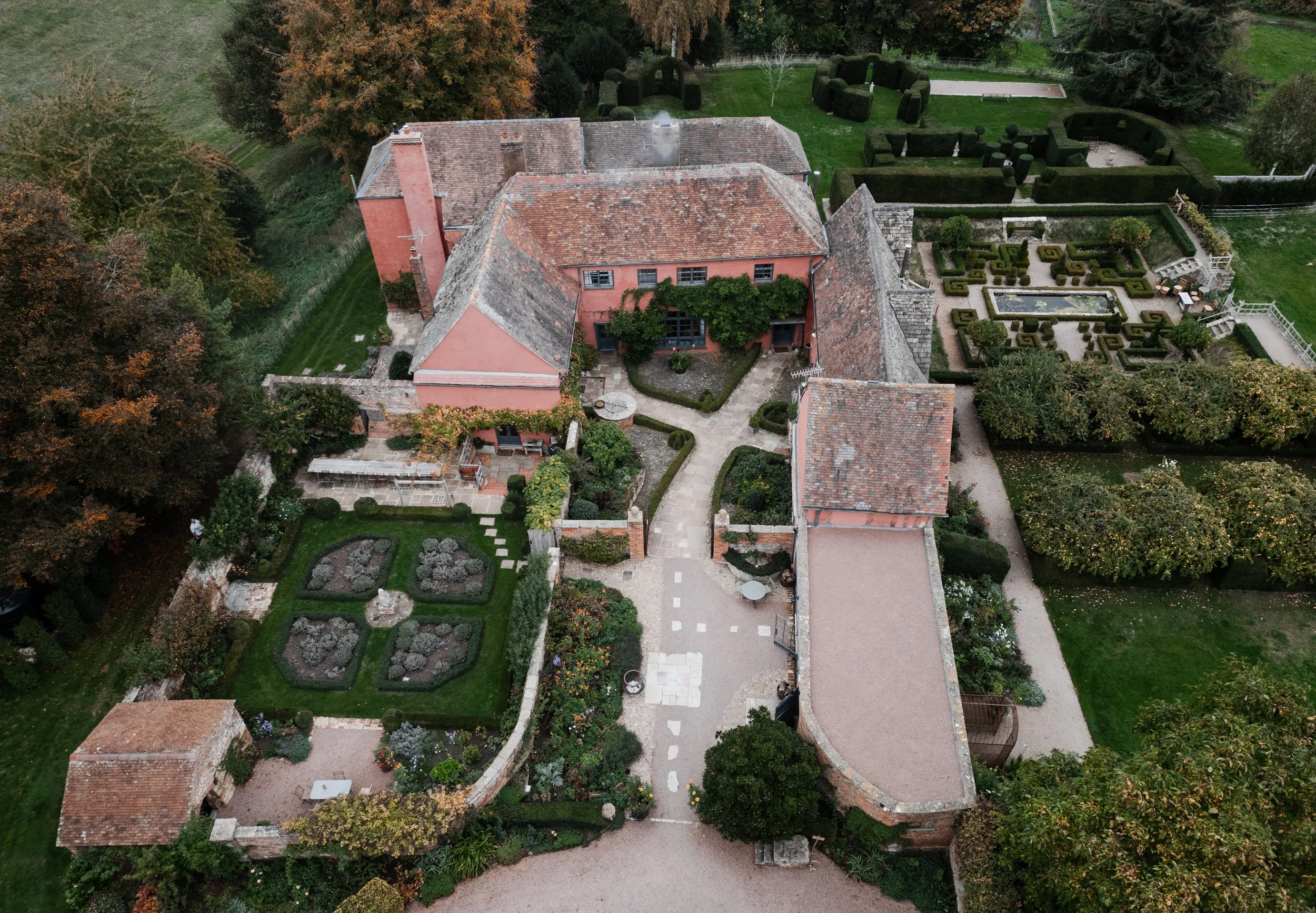 An aerial view of a historic brick house with a red tiled roof, surrounded by well-maintained gardens, hedges, and mature trees in an estate at sudeley castle, Gareth roy photography