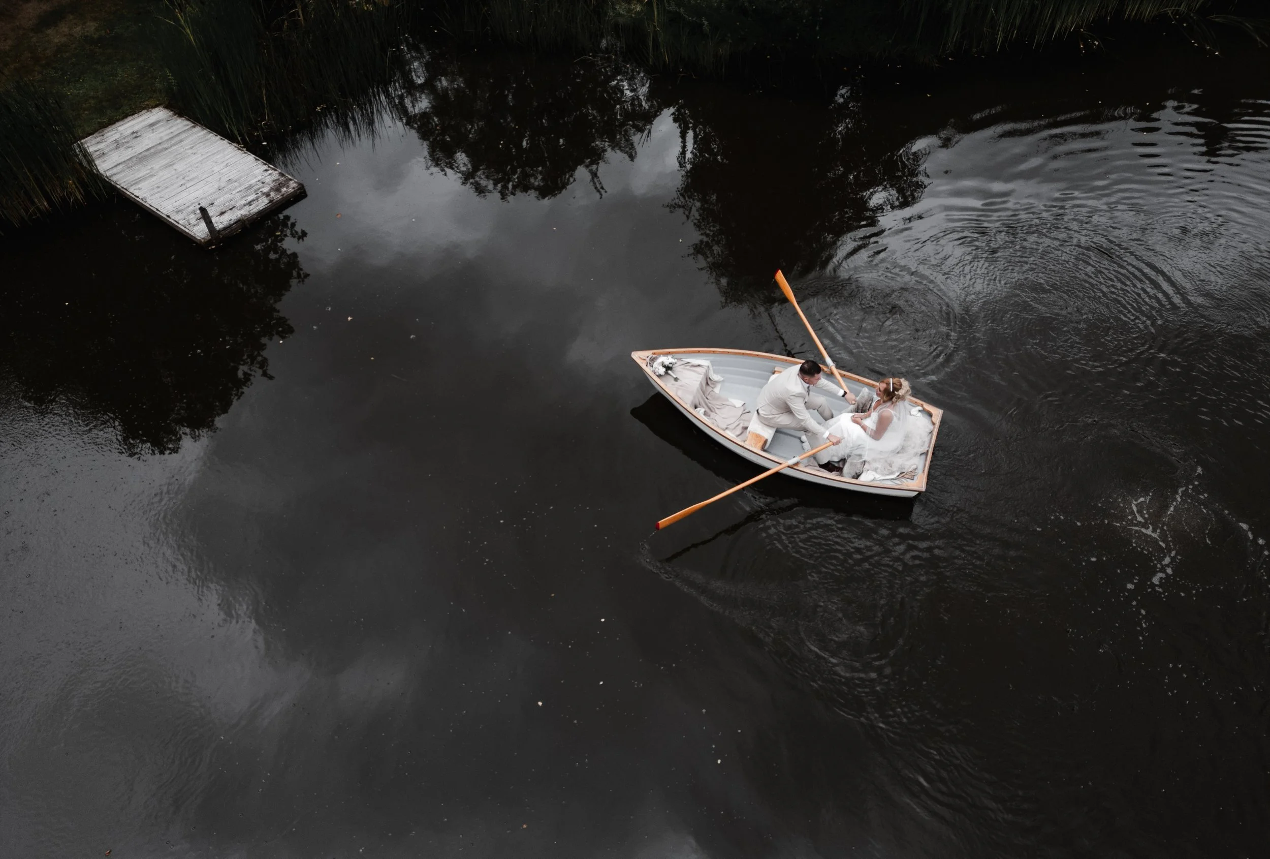 The Love Shack - Groom and bride in wedding attire, in a boat being photographed by a drone from above. 