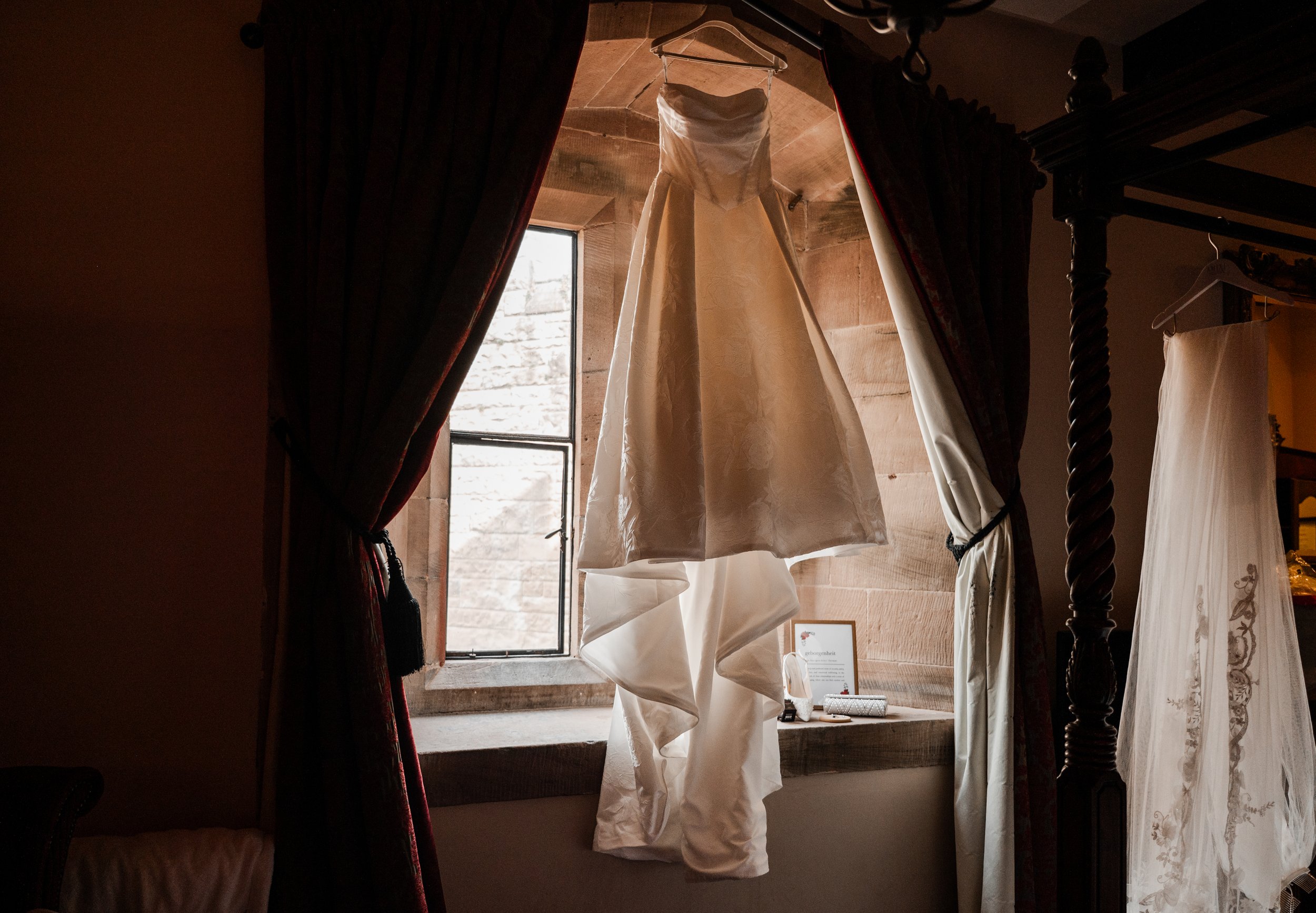 Peckforton Castle - wedding dress hung up in front of a large window