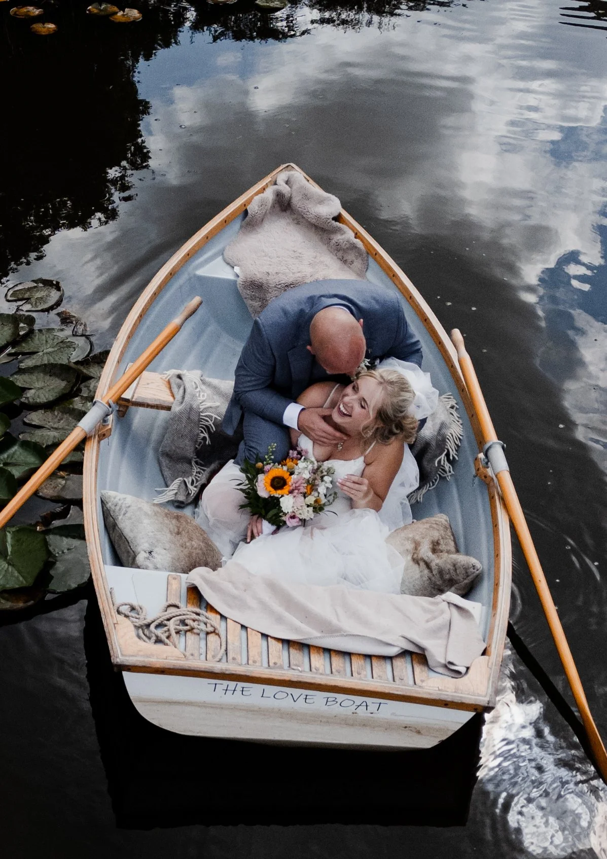 Couple in wedding attire sat in a rowing boat and laughing together