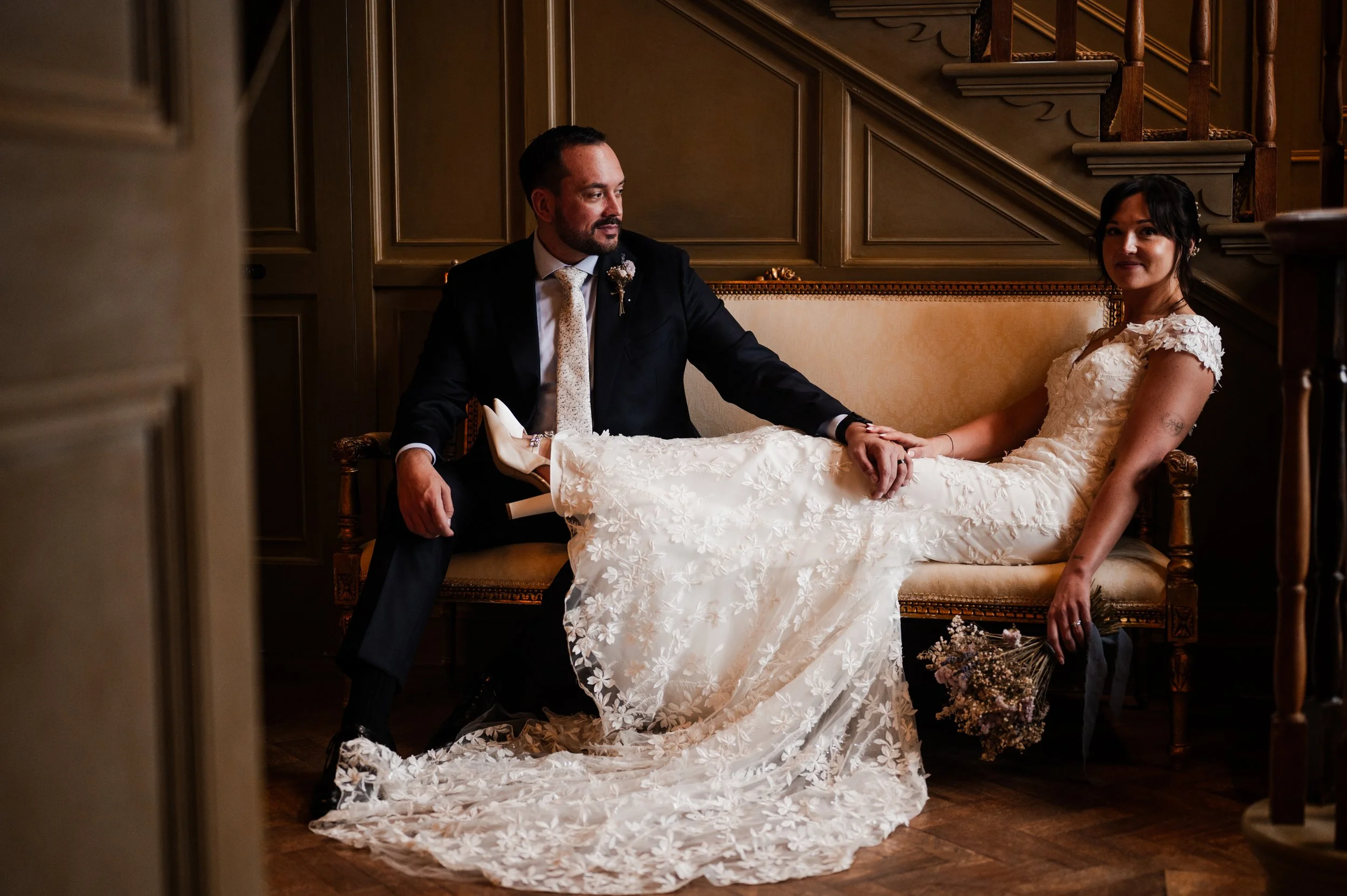 A couple in wedding attire sitting on a vintage sofa in an elegant, dimly lit room pauntley court, Gareth roy photography