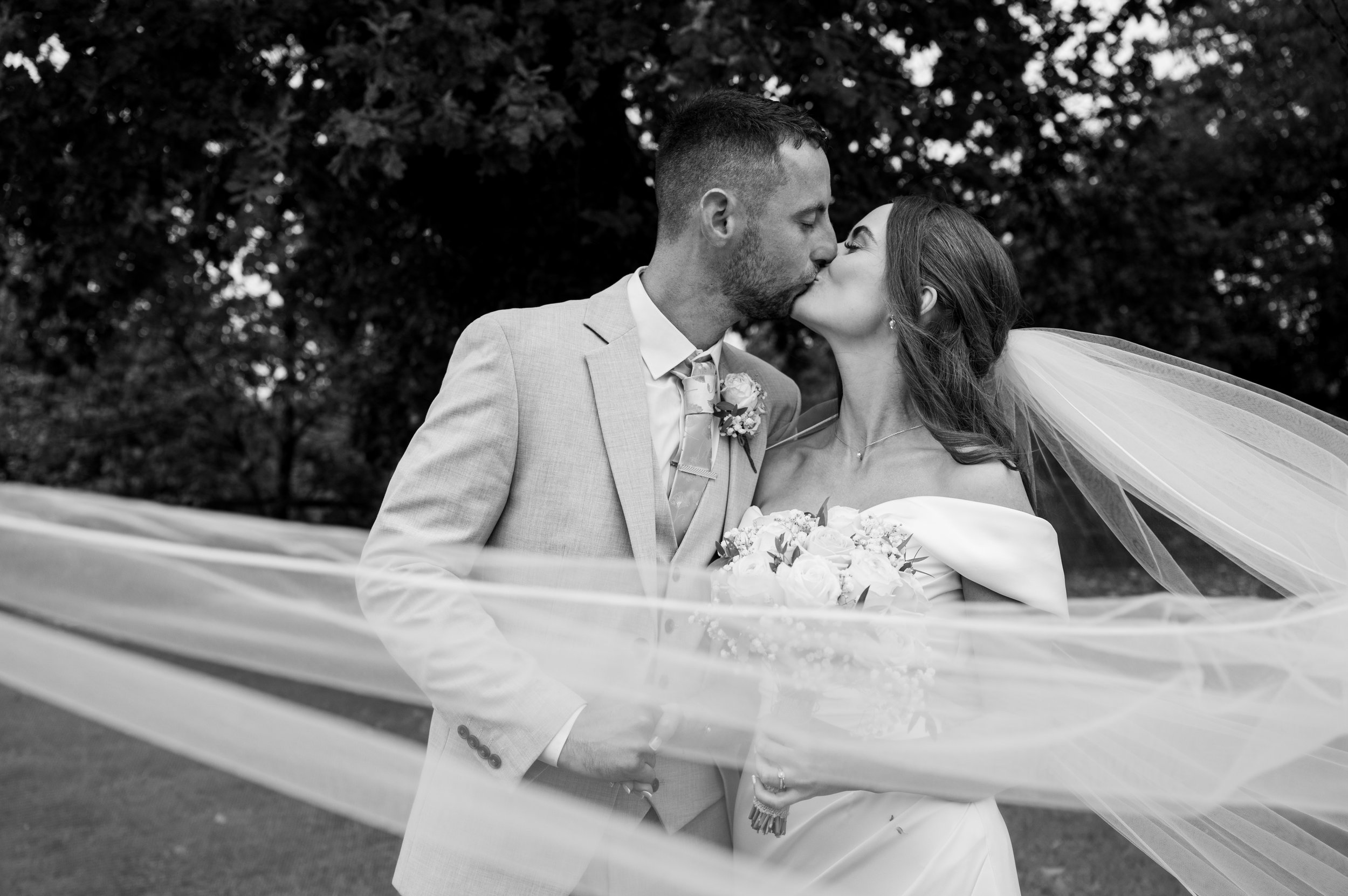 All Saint Church - black and white image of bride and groom in wedding attire kissing while veil is across the image