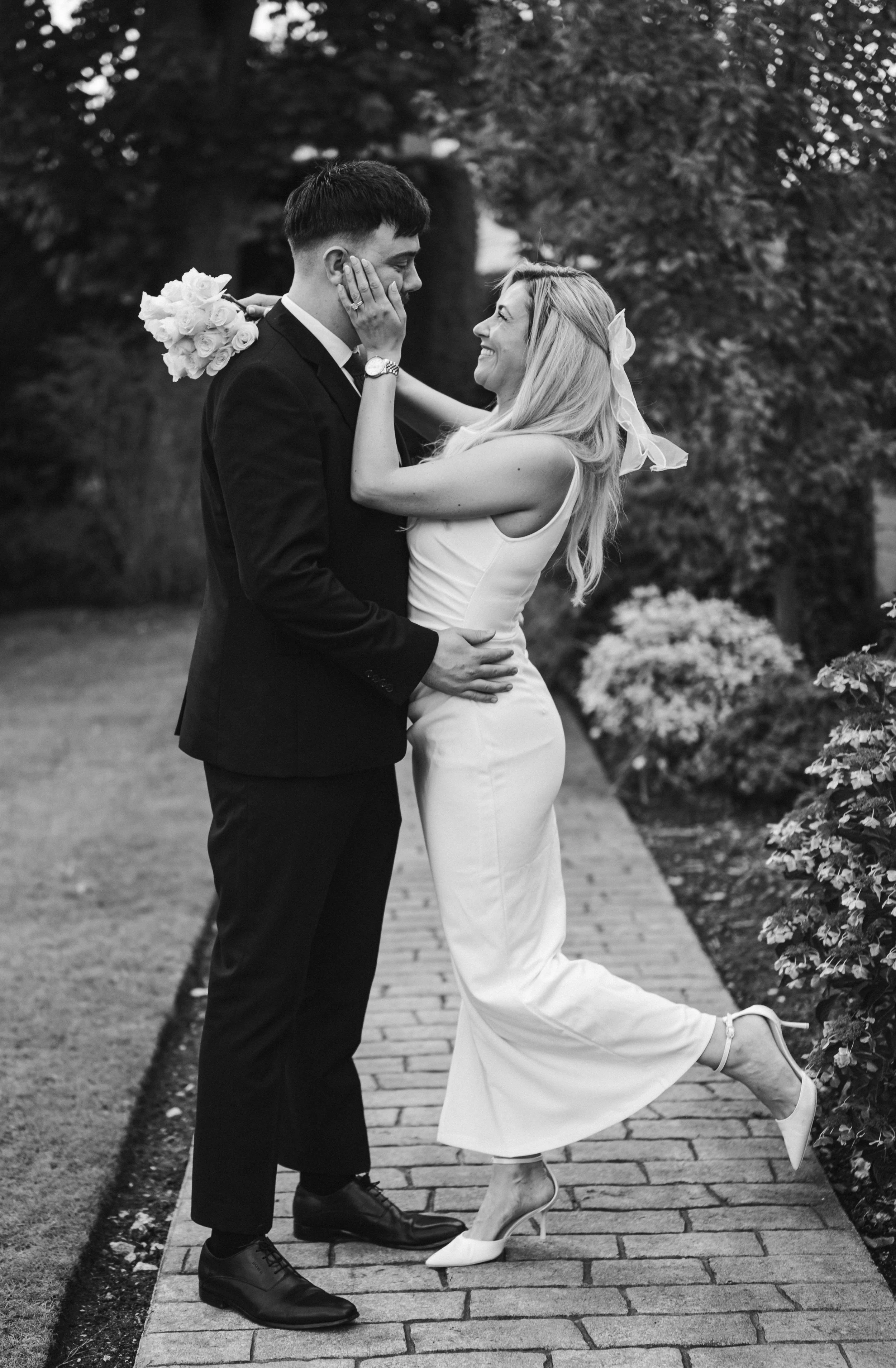 Black and white image of a bride and groom in an embrace on a garden path