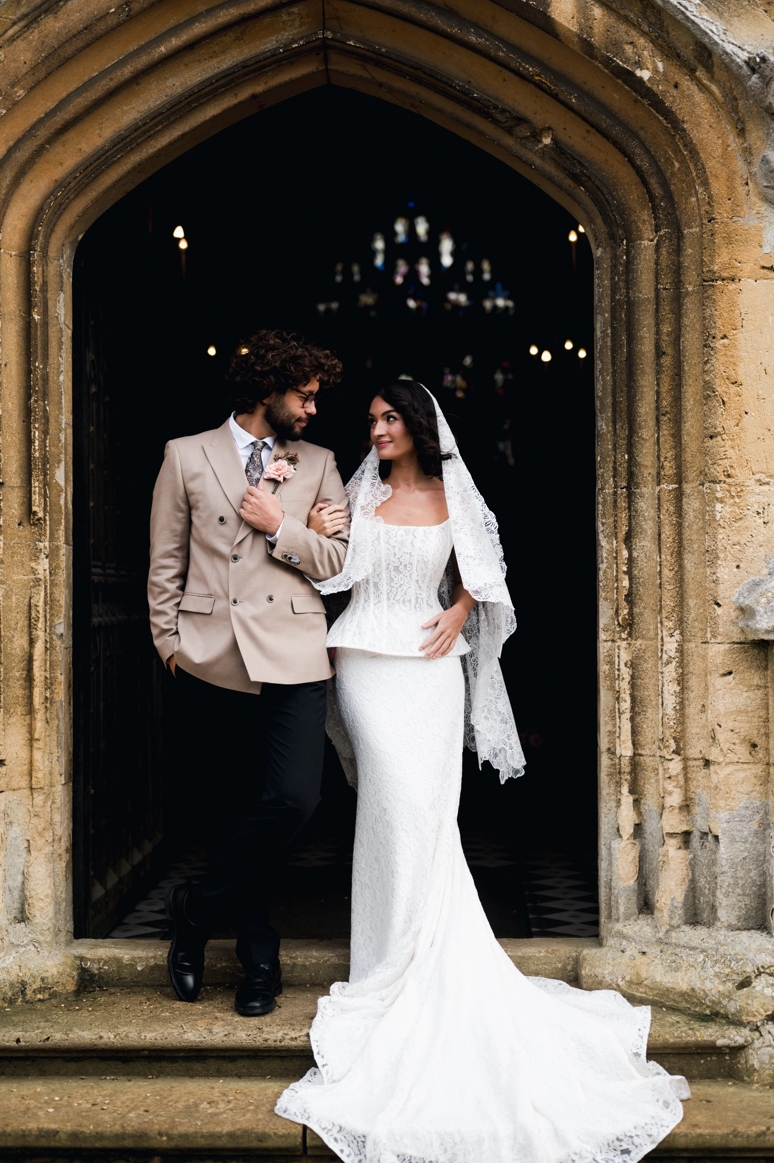 A bride and groom stand together under a stone archway, looking into each other's eyes inside a church at sudeley castle, Gareth roy photography