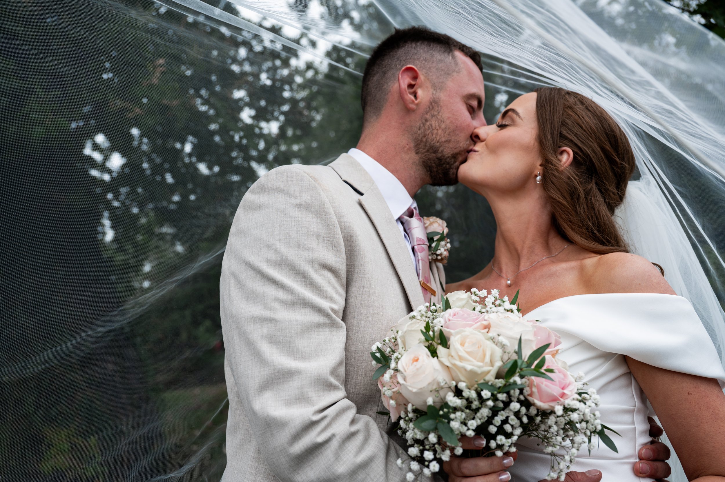 All Saint Church - bride and groom in wedding attire kissing while veil is over them 