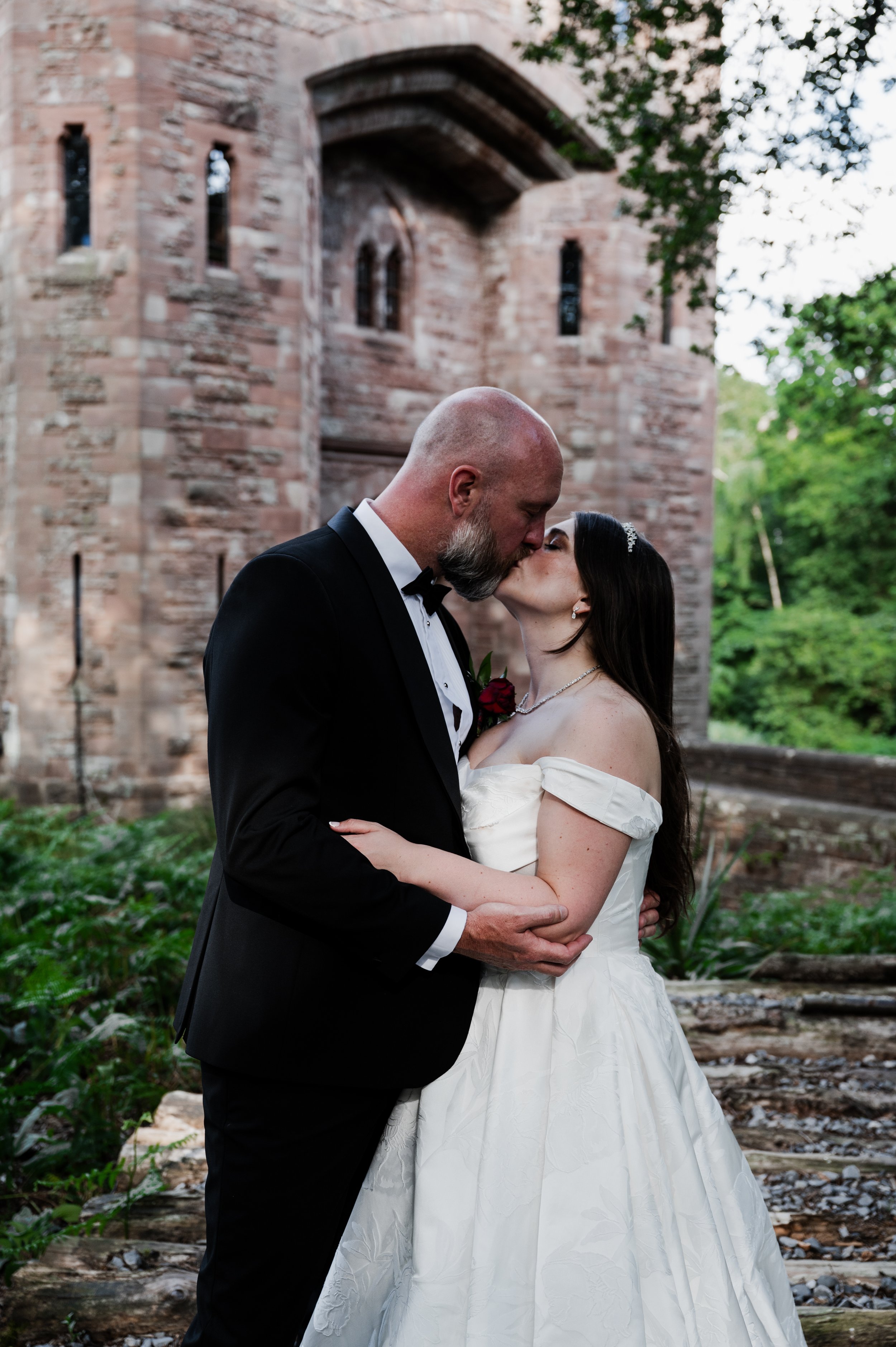 Peckforton Castle - bride and groom in wedding attire kissing in front of Peckforton Castle
