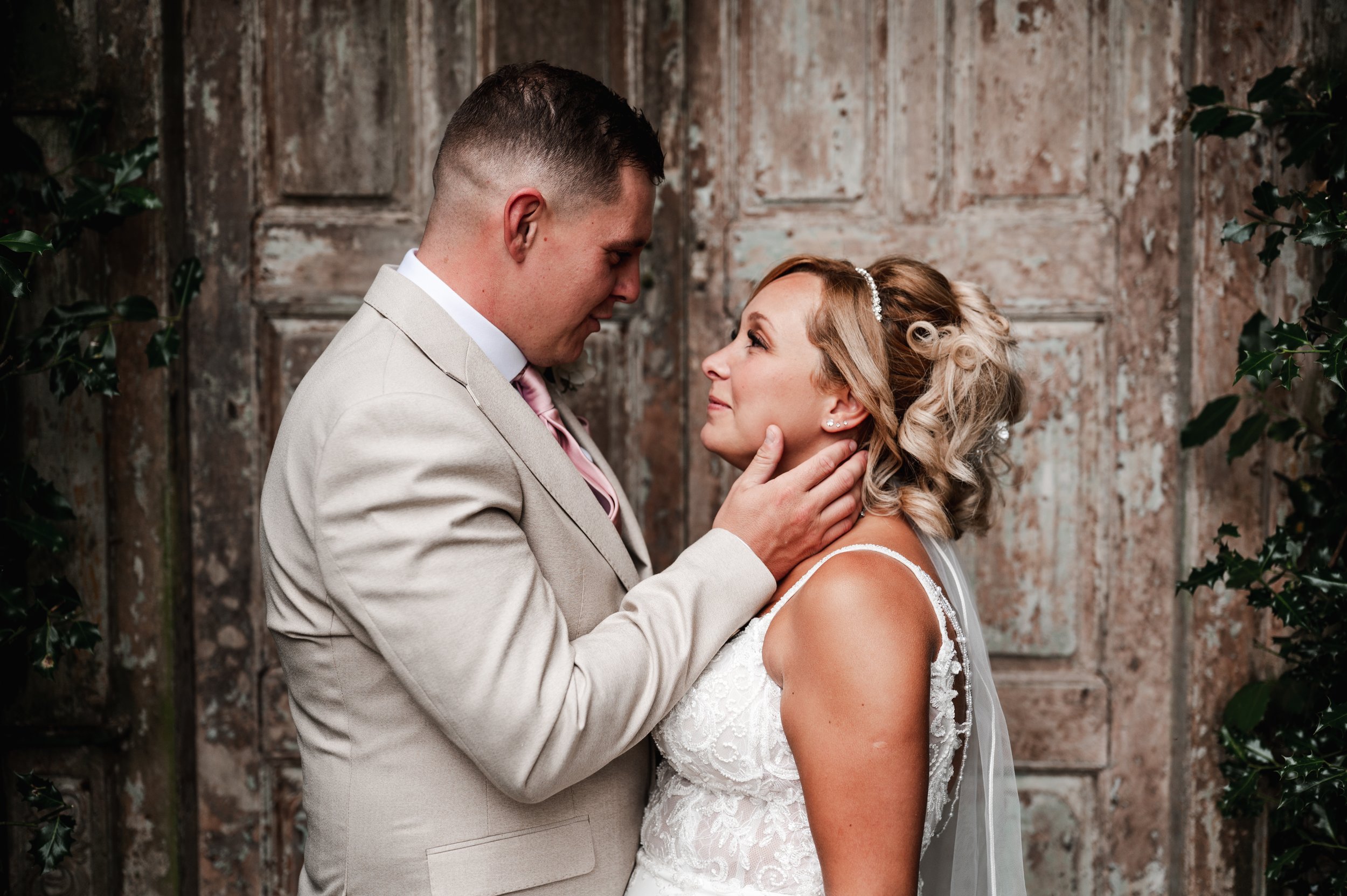 The Love Shack - groom and bride in wedding attire, looking at each other and smiling in front of a wooden door. 