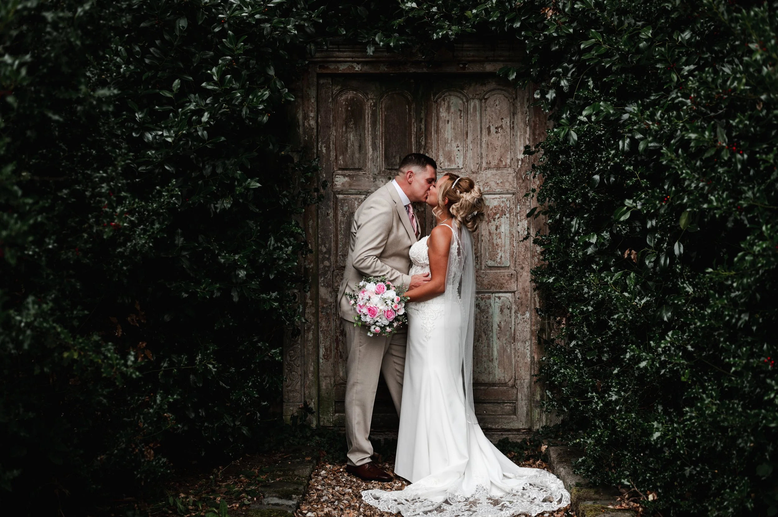 The Love Shack - groom and bride in wedding attire, looking at each other and smiling in front of a wooden door. 