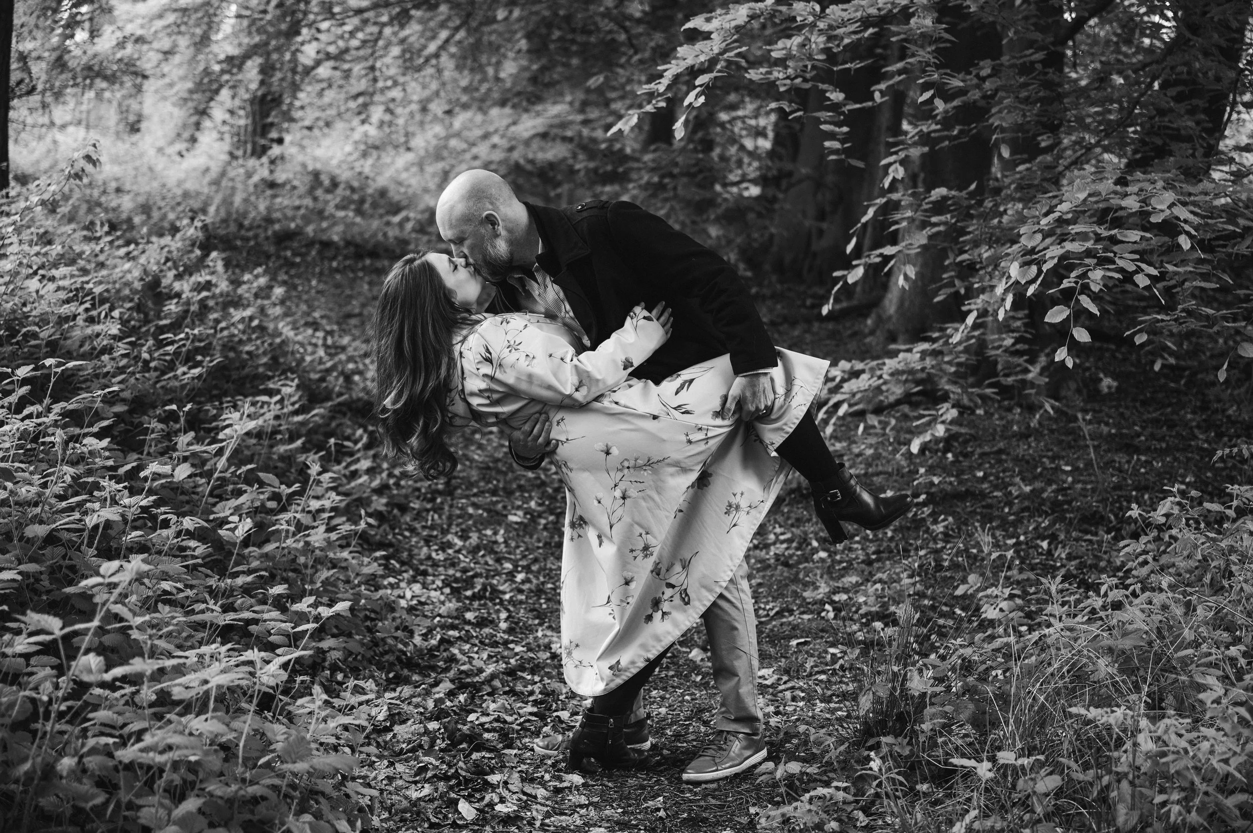 Delamere Forest Engagement shoot - black and white image of man dipping woman into a kiss while surrounded by woodland