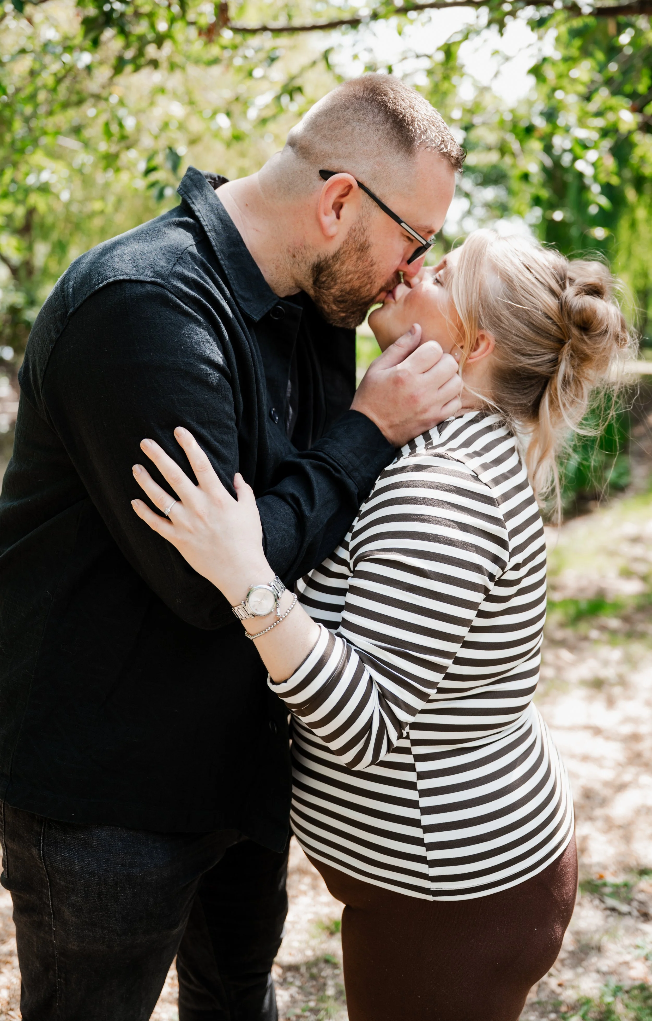 The Grosvenor Pulford Engagement - man in black shirt and woman in striped top, kissing and surrounded by trees