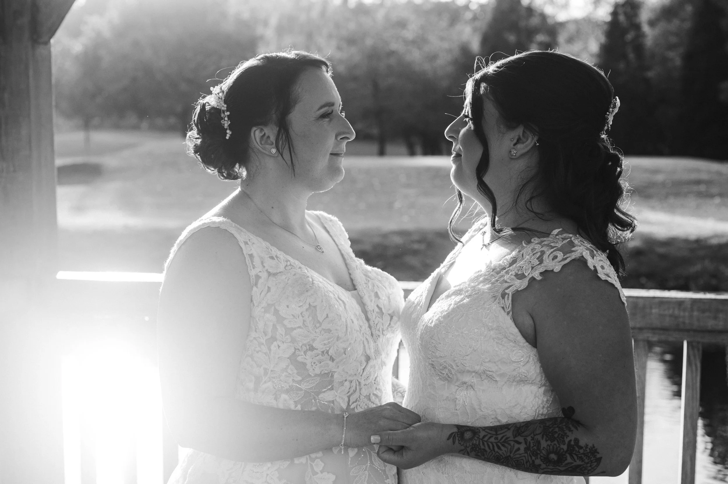 Cheshire Wedding Photographer - Black and white images of two brides holding hands and smiling at each other with the background of a lake and trees