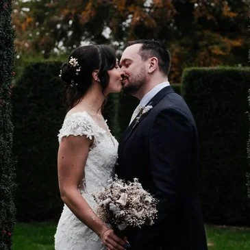 Image of bride and groom in wedding attire kissing in historical gardens