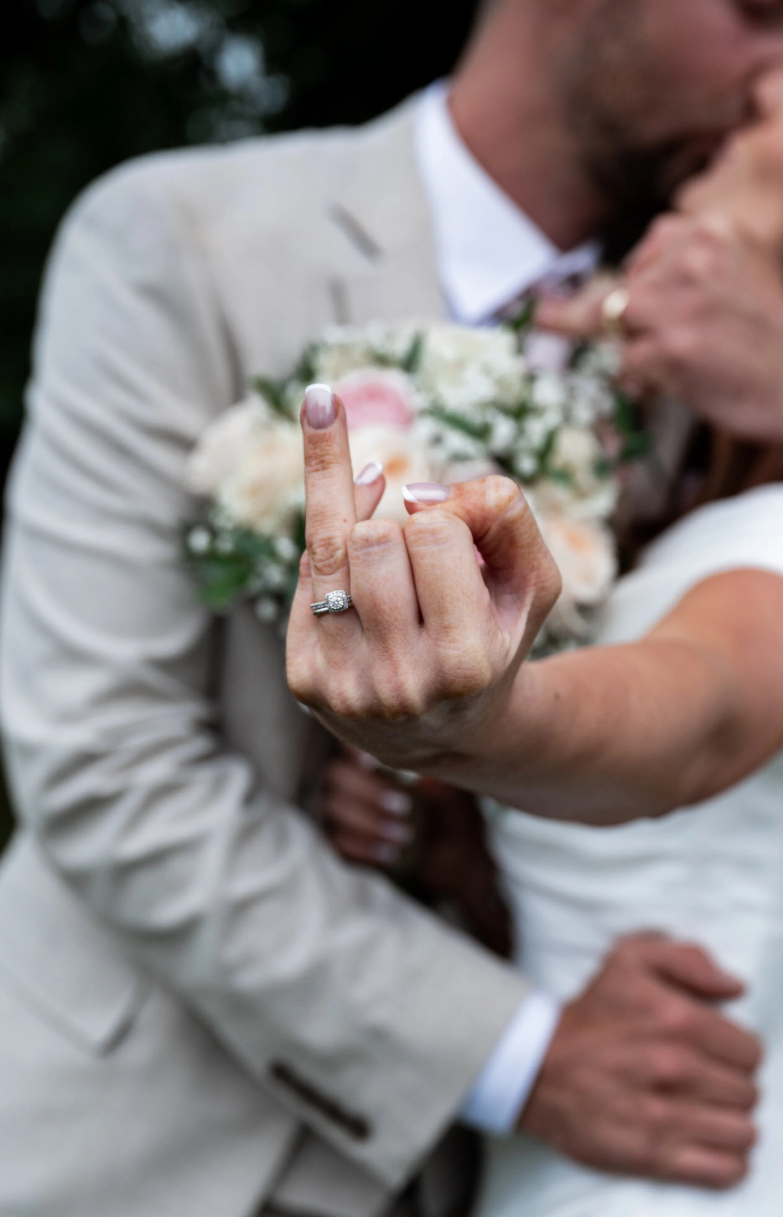 All Saint Church - bride and groom in wedding attire kissing while bride puts up her finger to the camera showing her engagement ring and wedding band