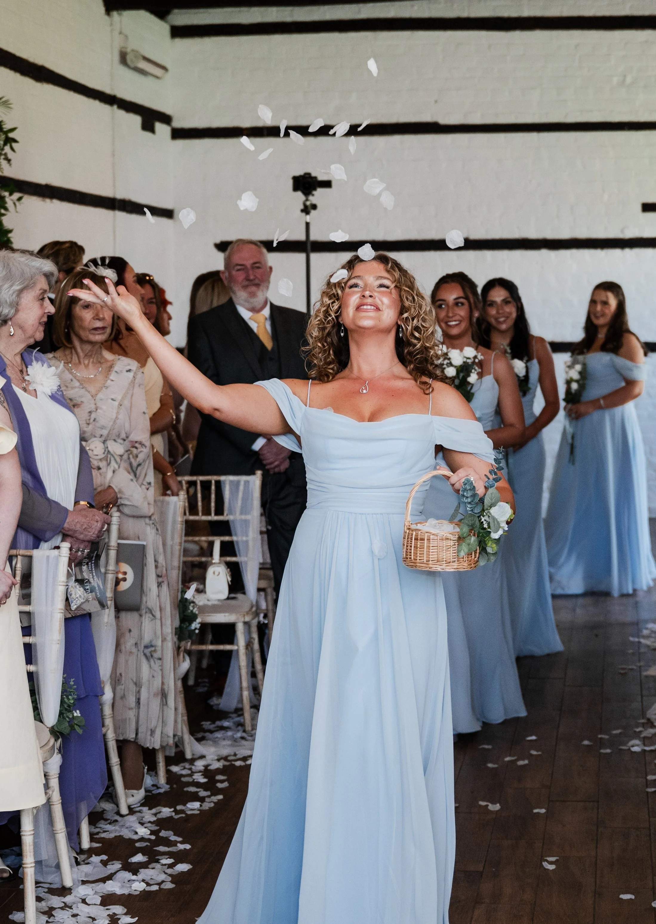 A bridesmaid is pictured wearing a light blue dress, throwing white petals over her