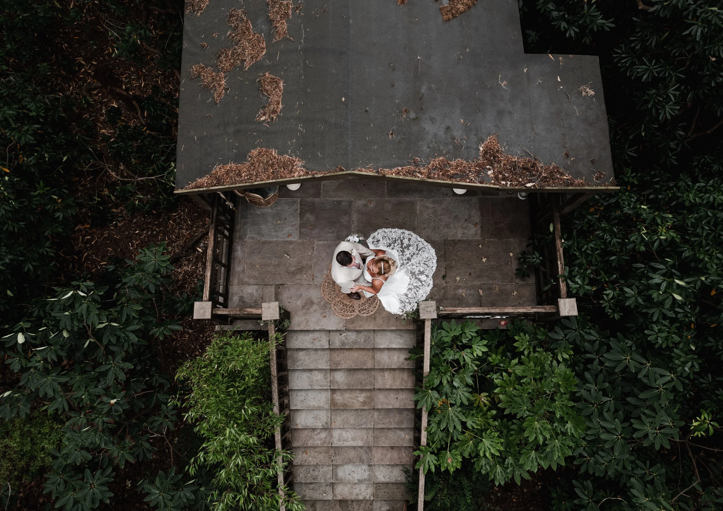 The Love Shack - Bird eye drone image of groom and bride in wedding attire, stood on top of a wooden staircase.