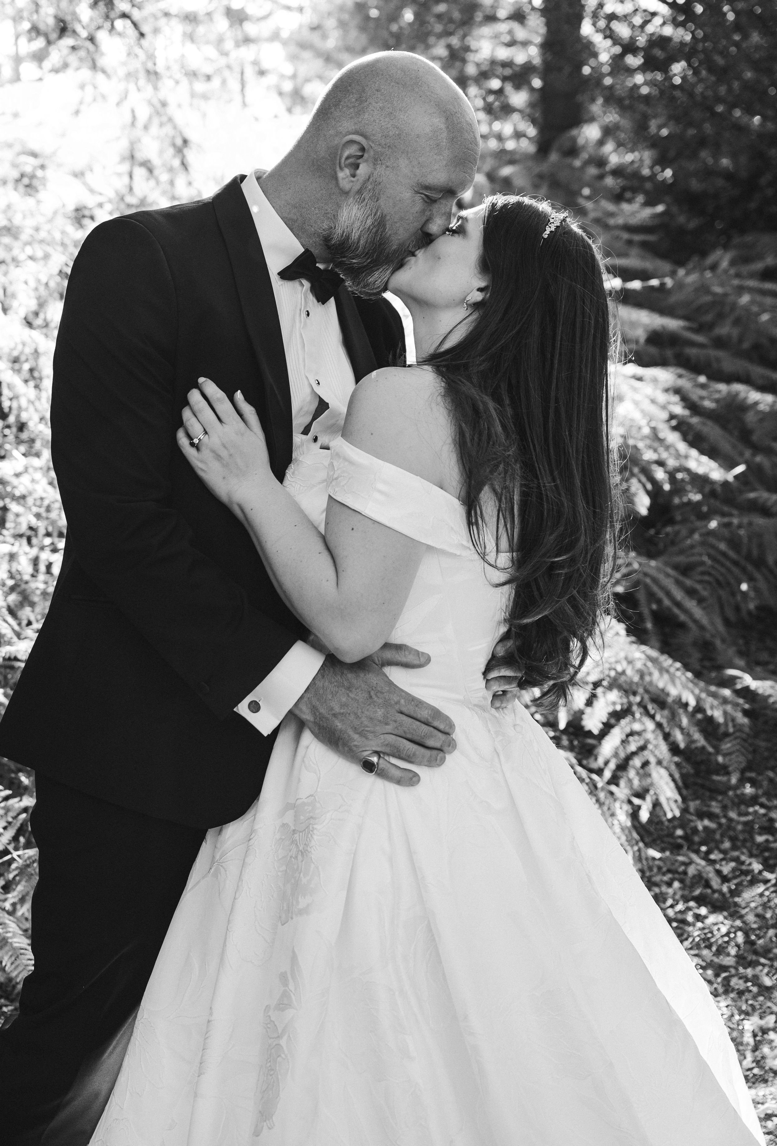 Peckforton Castle - Black and white image of bride and groom in wedding attire kissing in woodlands