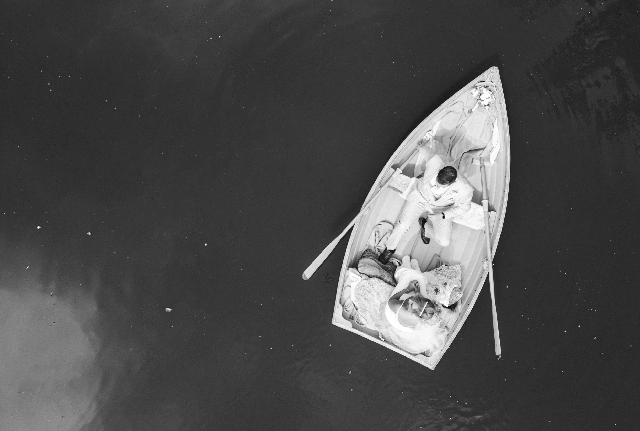 The Love Shack - Black and white image of groom and bride in wedding attire being pictured from above in a small boat