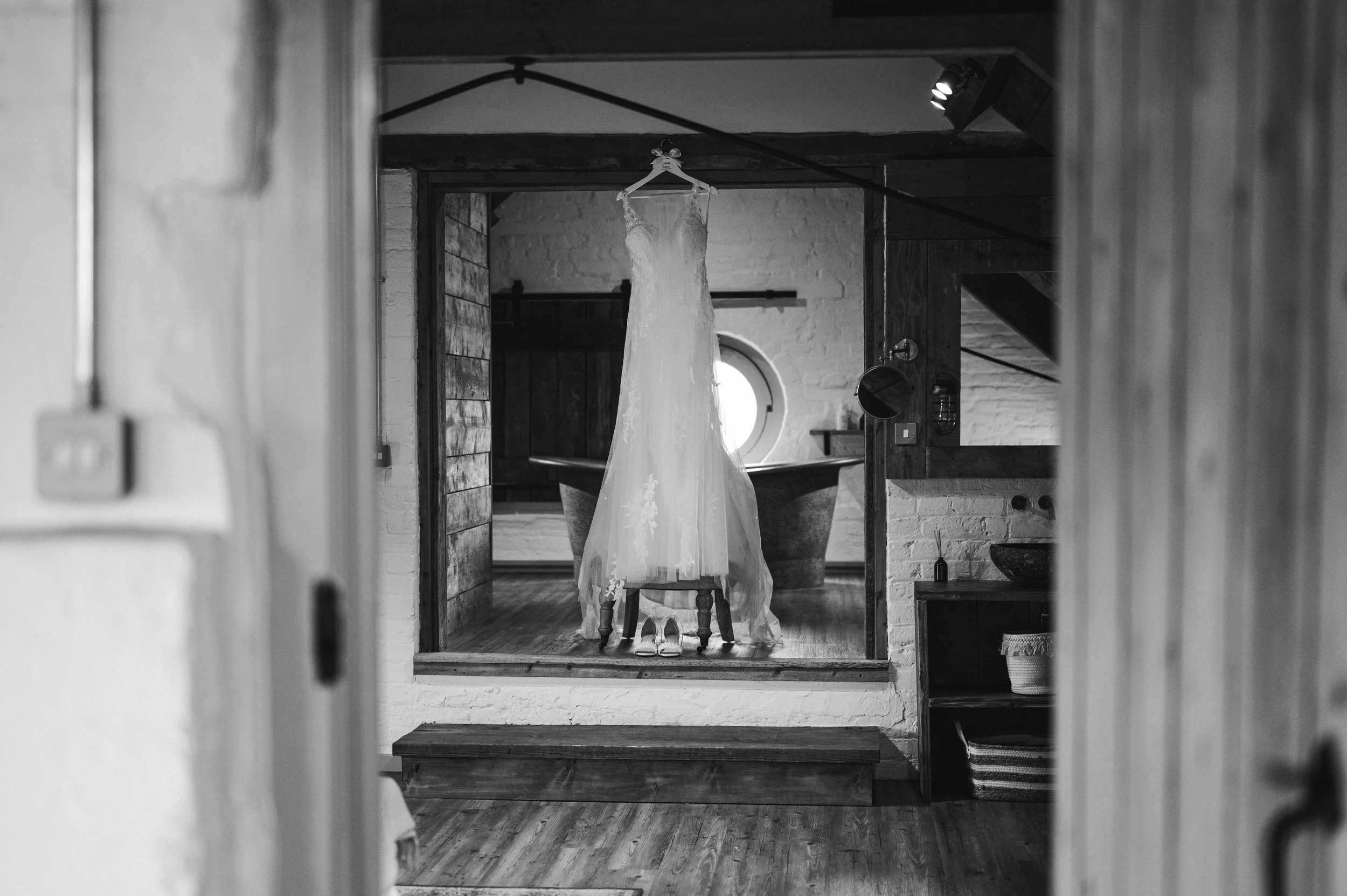 Wedding dress hanging in front of a bathtub in rustic bridal suite with wood and brick interior grange barn Whitchurch, Gareth roy photography