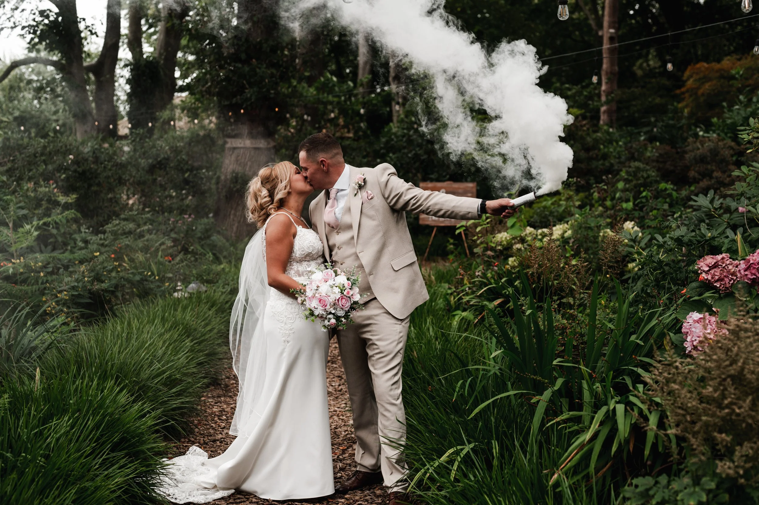 The Love Shack - Groom and bride in wedding attire, kissing while groom holds a white smoke flare. 