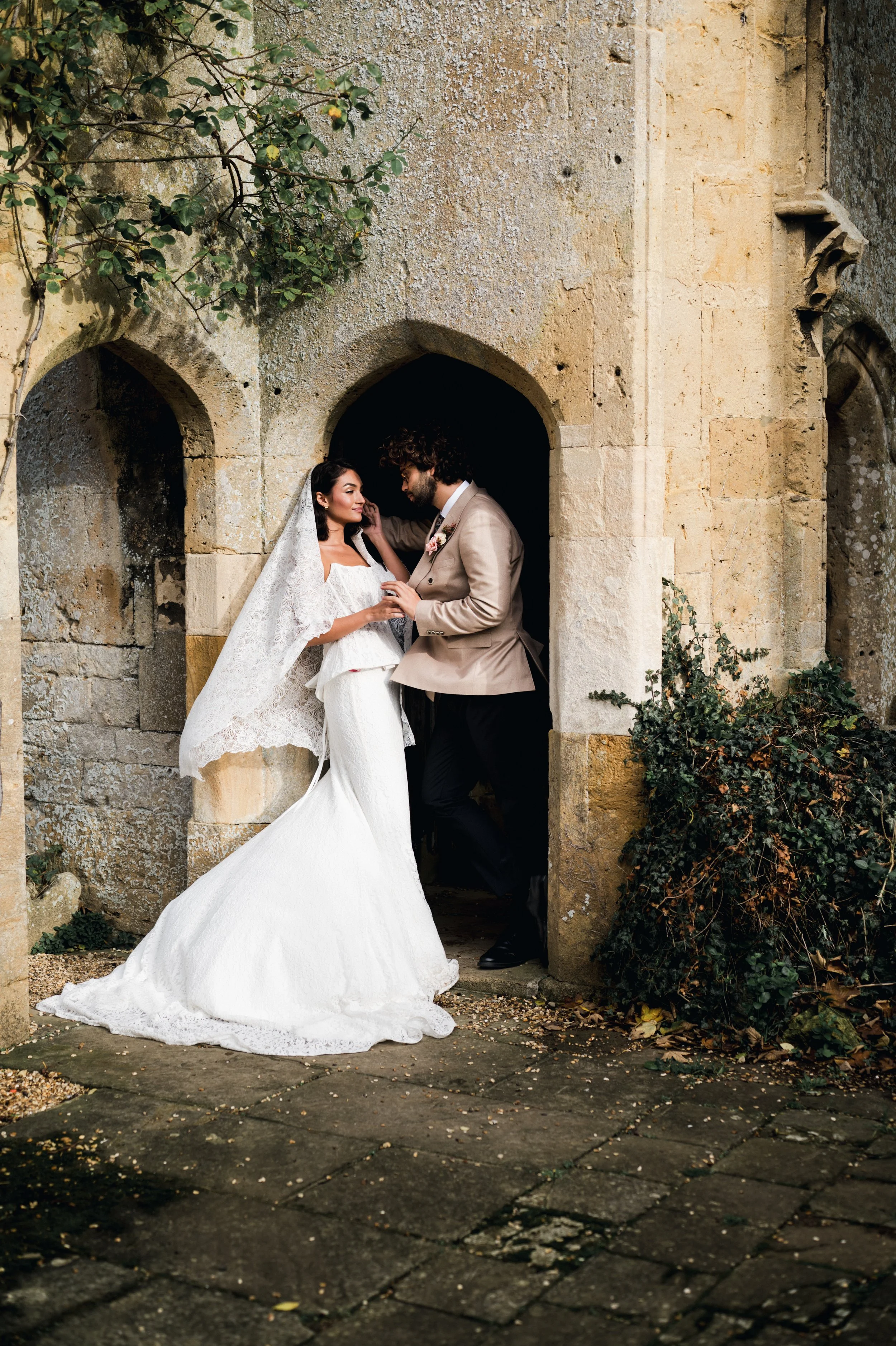 Bride and groom sharing a moment at a rustic stone archway, surrounded by greenery, on their wedding day at sudeley castle, Gareth roy photography