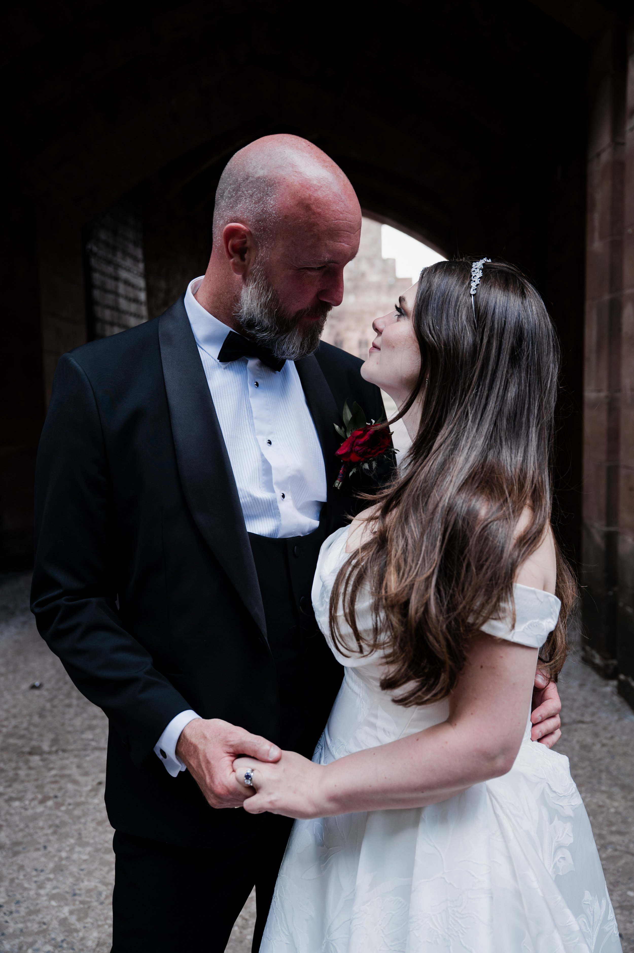 Peckforton Castle - bride and groom in wedding holding each others hands in an archway