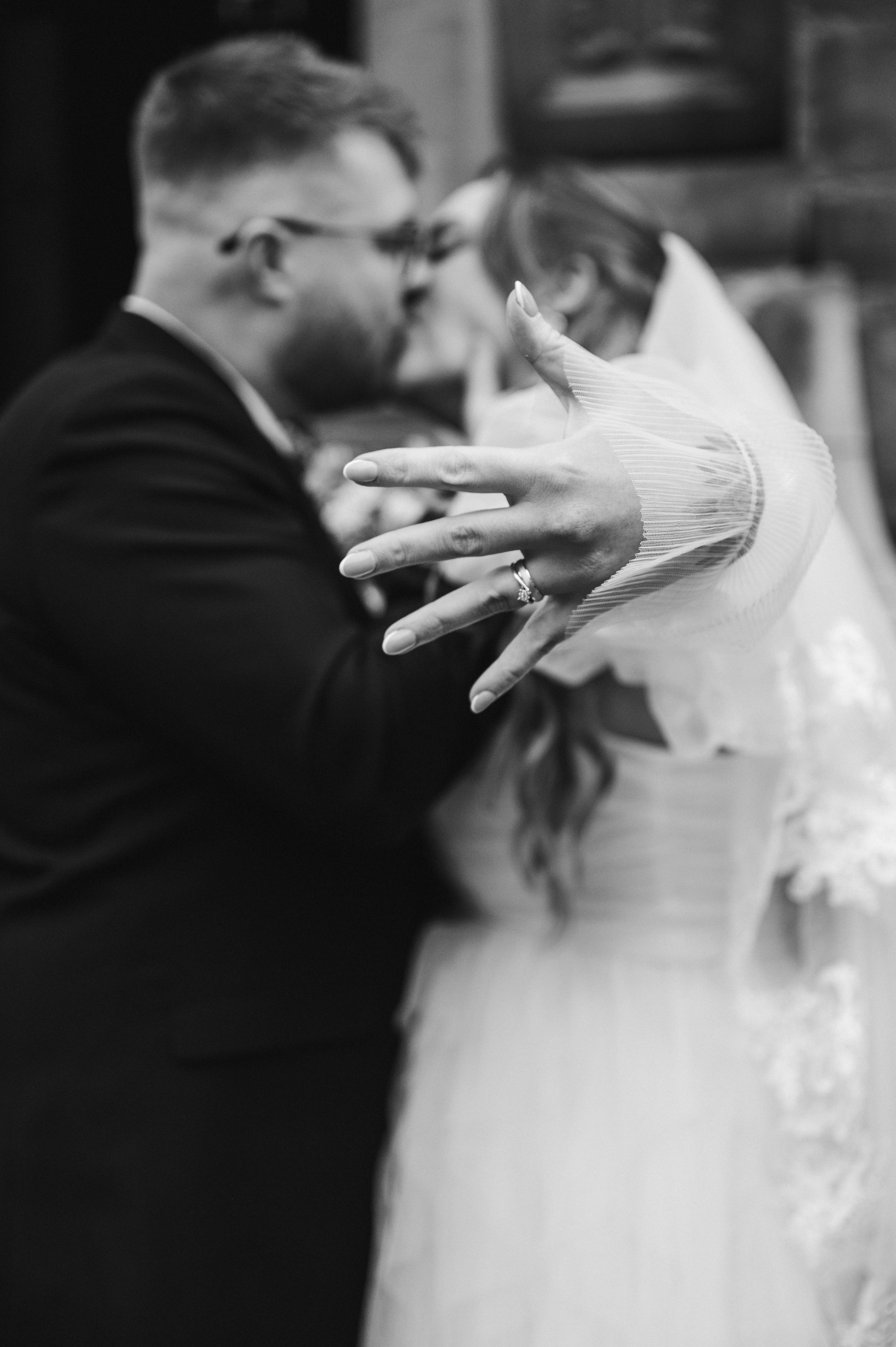 Black and white image of a bride and groom kissing and the bride showing her new wedding hand on her hand. 