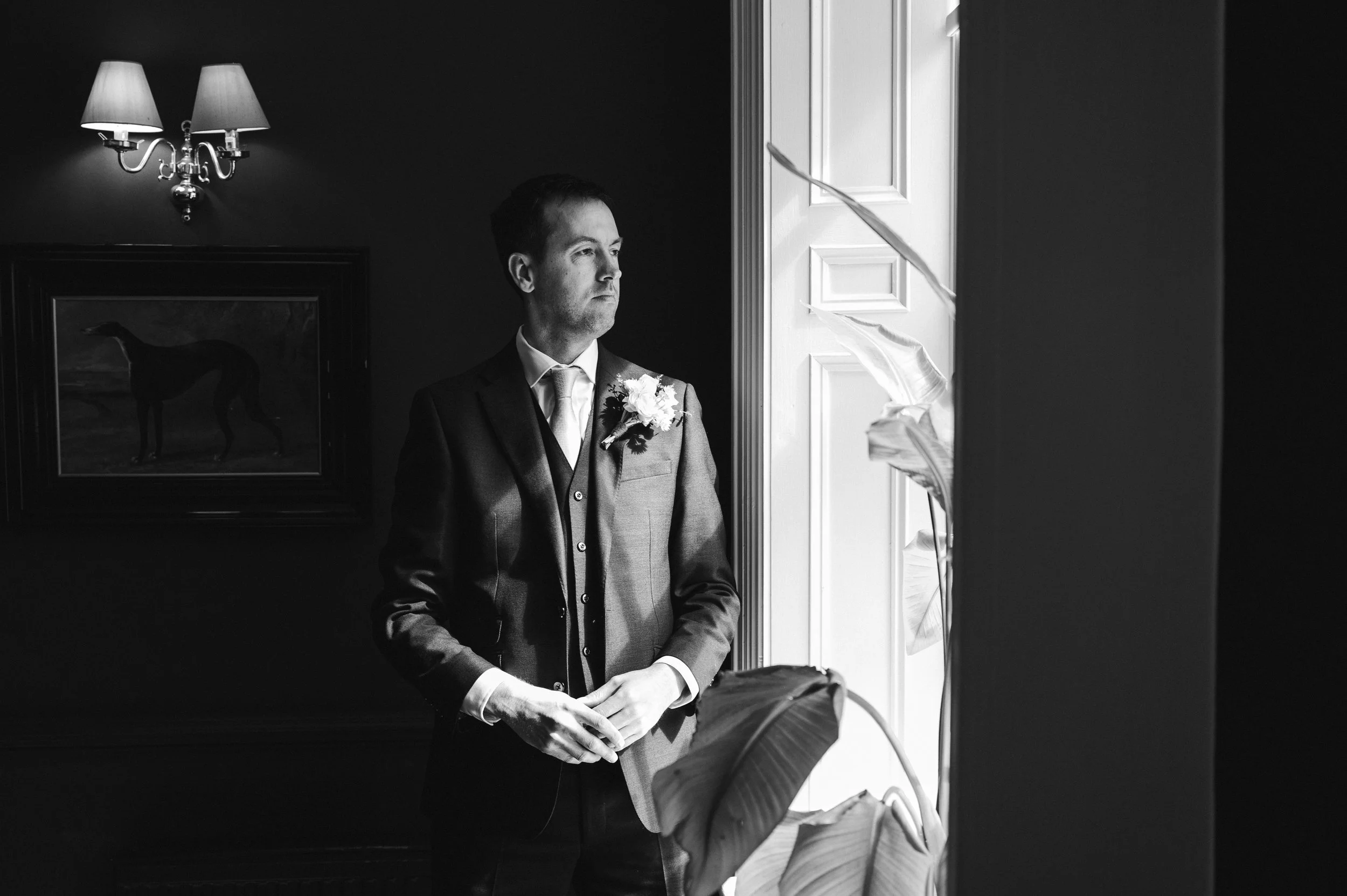 Wedding Photographer Cheshire - Black and white image of a groom in a suit looking out of the window. 