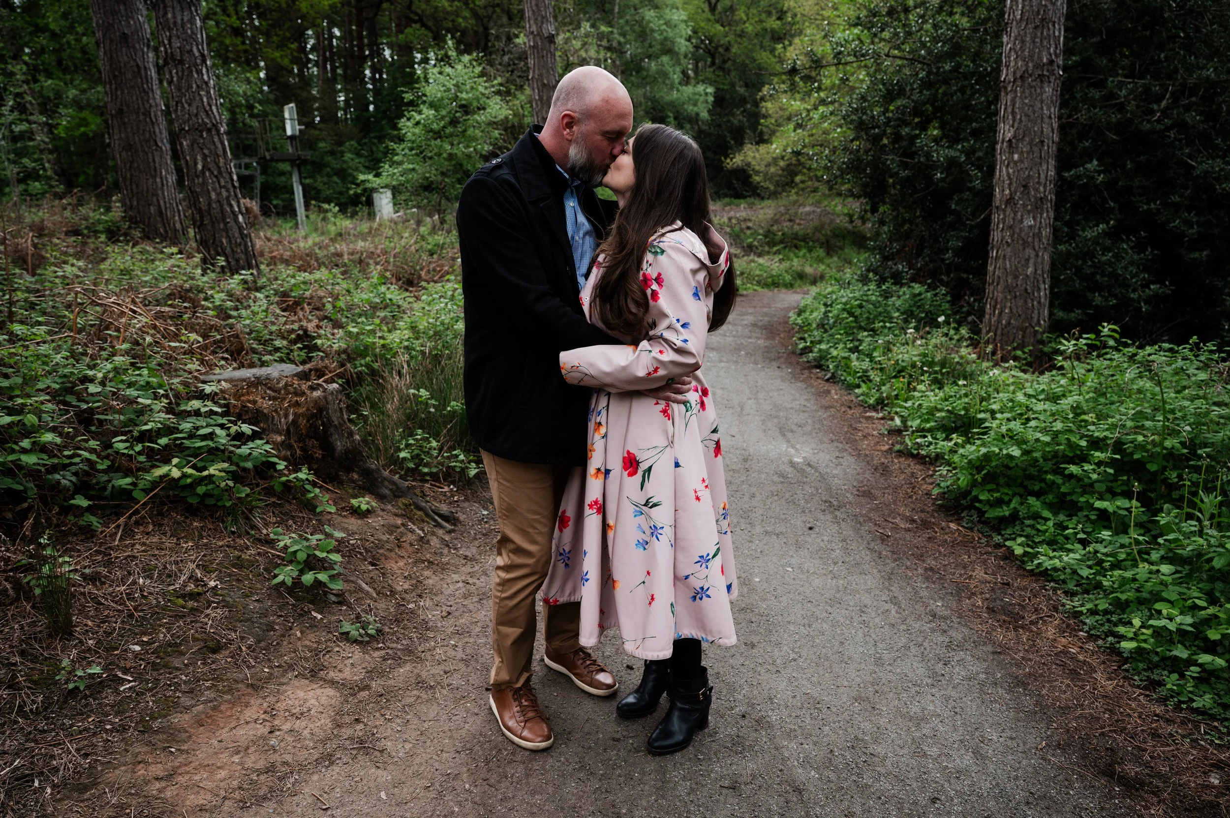 Delamere Forest Engagement shoot - man and woman embraced and kissing on a path with woodland behind them