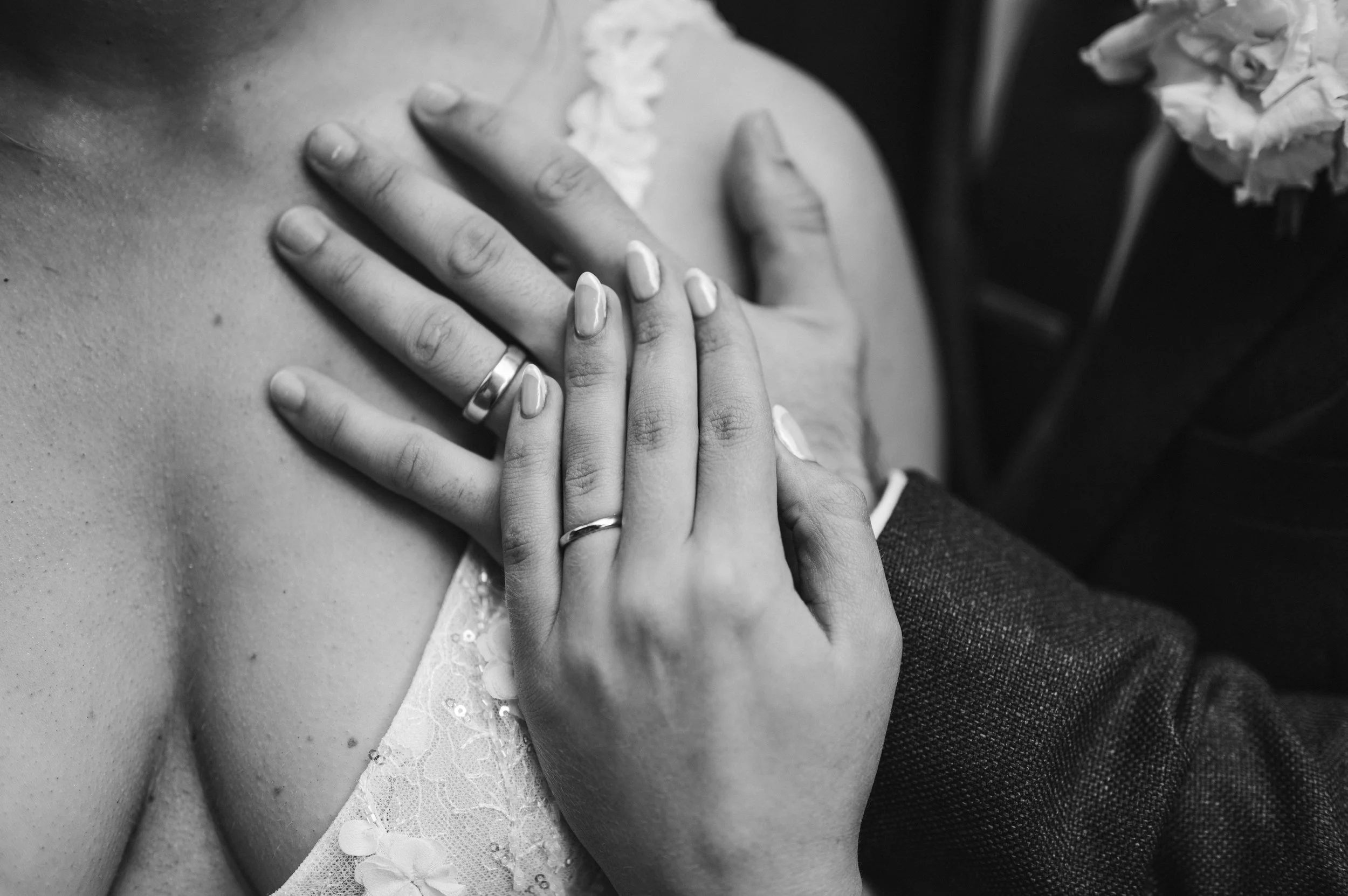 Close-up of two hands sharing wedding rings, placed on a woman's shoulder, with delicate lace fabric visible on her dress in black and white hidden river cabins, Gareth roy photography