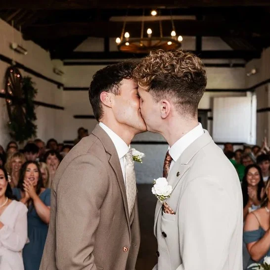 Image of two grooms at Lillibrooke Manor in wedding attire kissing at the end of a wedding ceremony