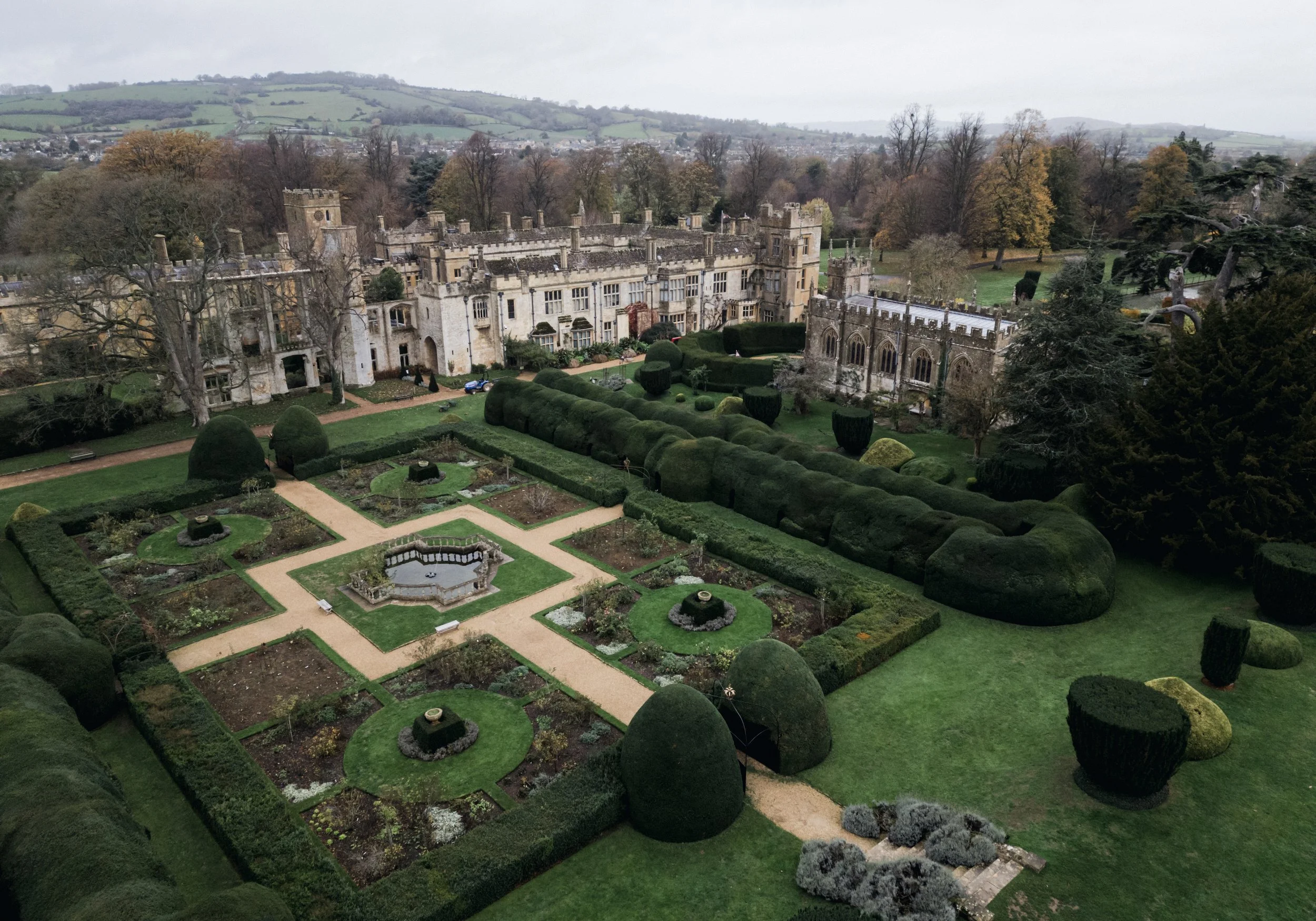 A historic castle with adjacent gardens featuring manicured hedges, flower beds, and pathways, set against a backdrop of rolling hills and trees at sudeley castle, Gareth roy photography