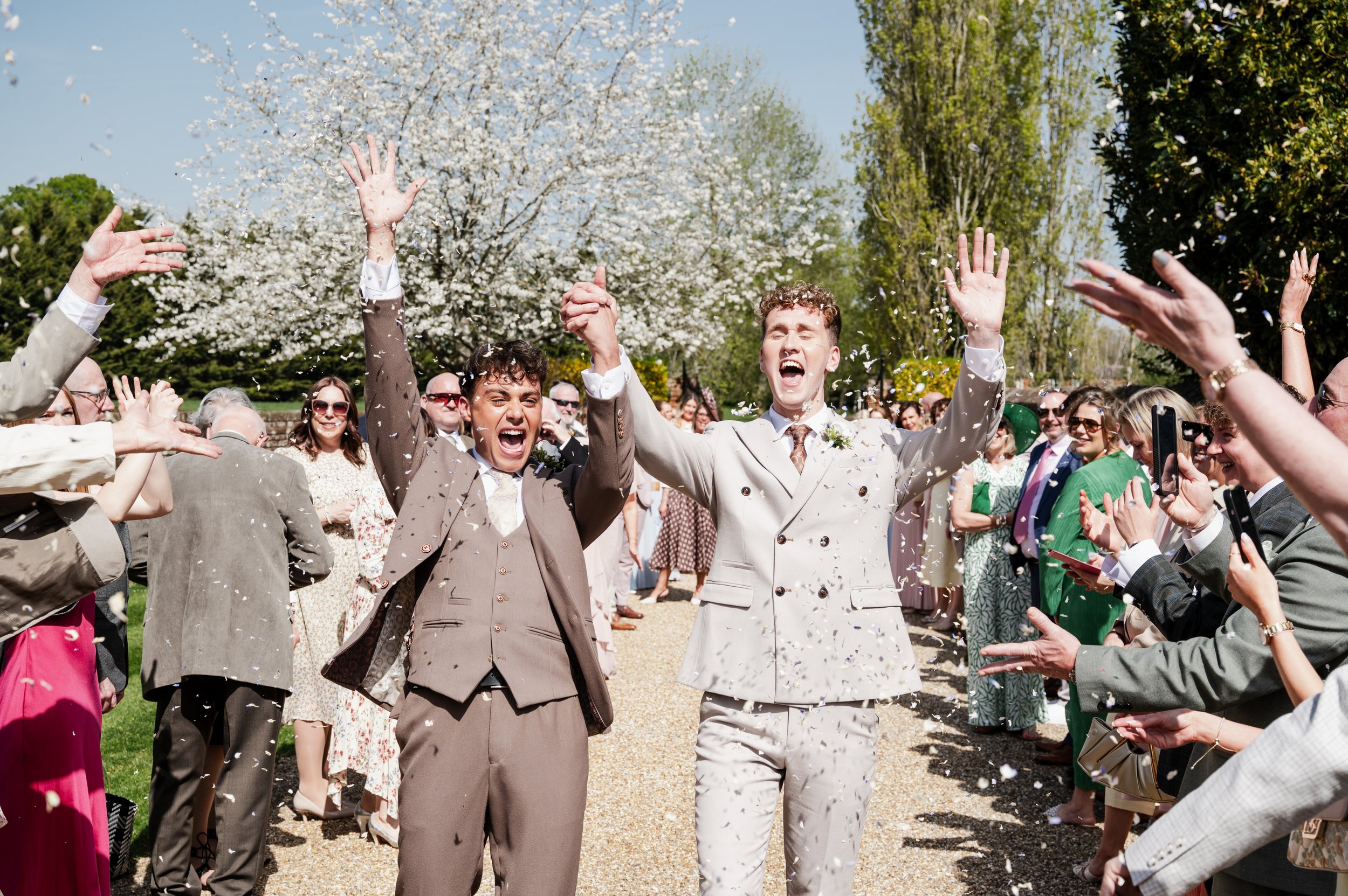 Two grooms celebrate as confetti is thrown on them by family and friends