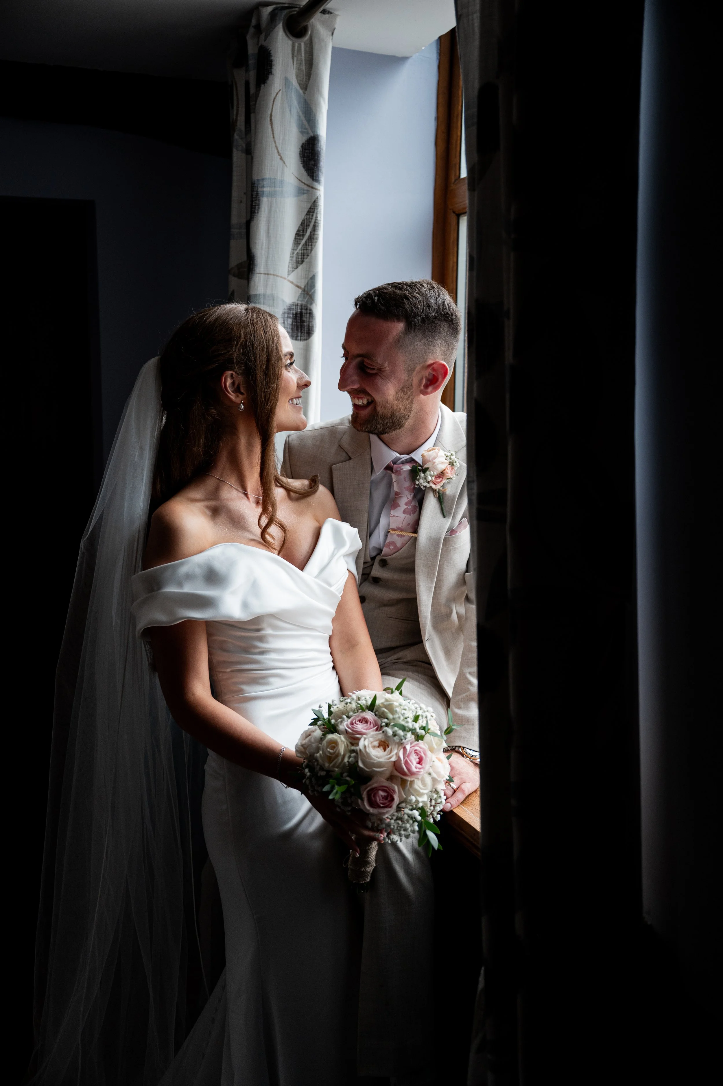 All Saint Church - bride and groom in wedding attire sat in a bay window and smiling together