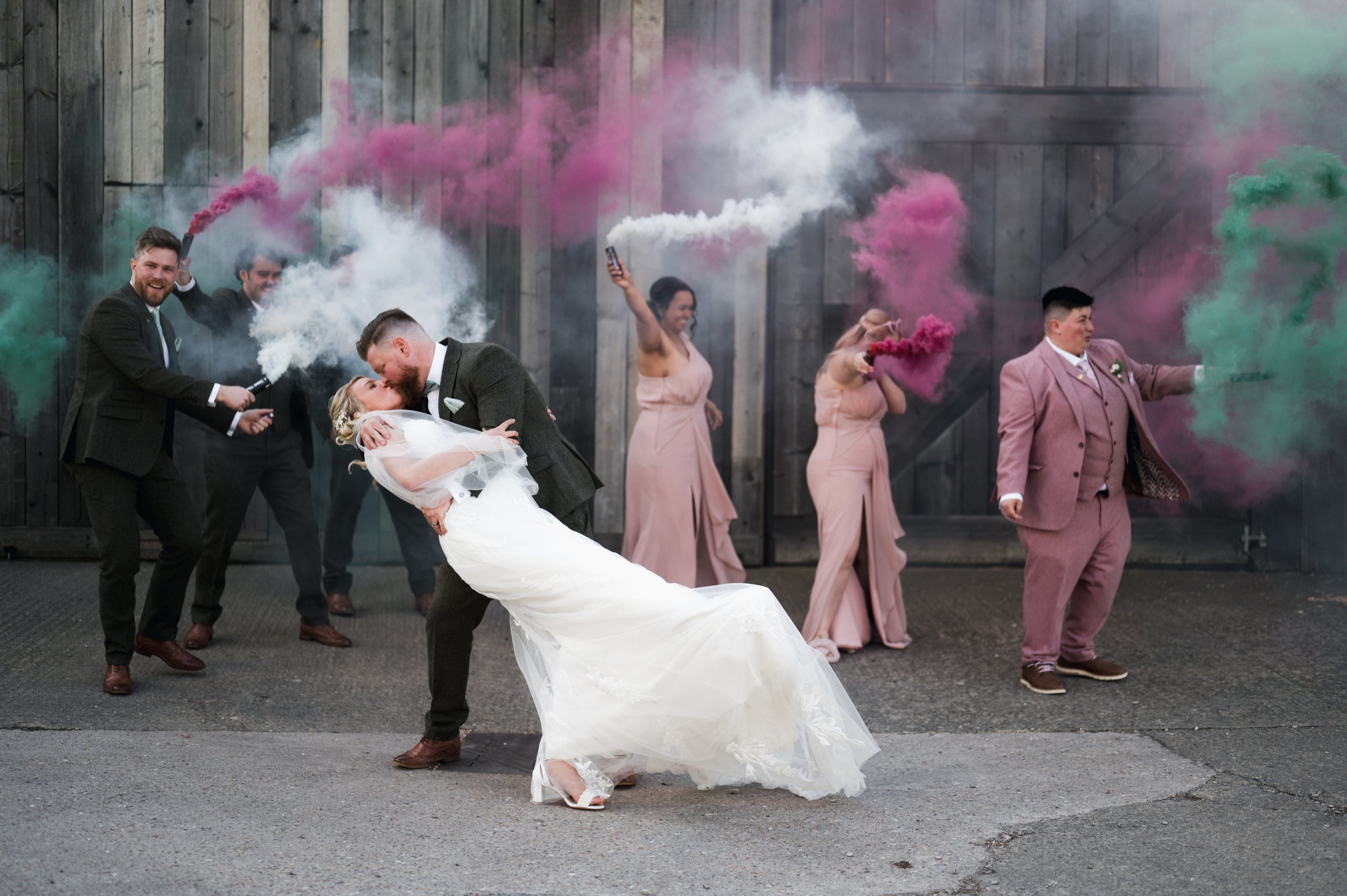 Groom dips bride for a kiss during a wedding celebration with friends holding colored smoke canisters grange barn Whitchurch, Gareth roy photography
