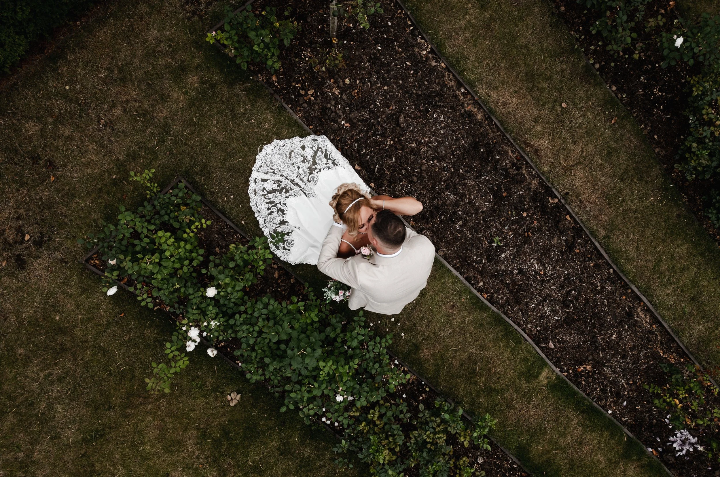 The Love Shack - Drone image of groom and bride in wedding attire, in gardens and kissing. 