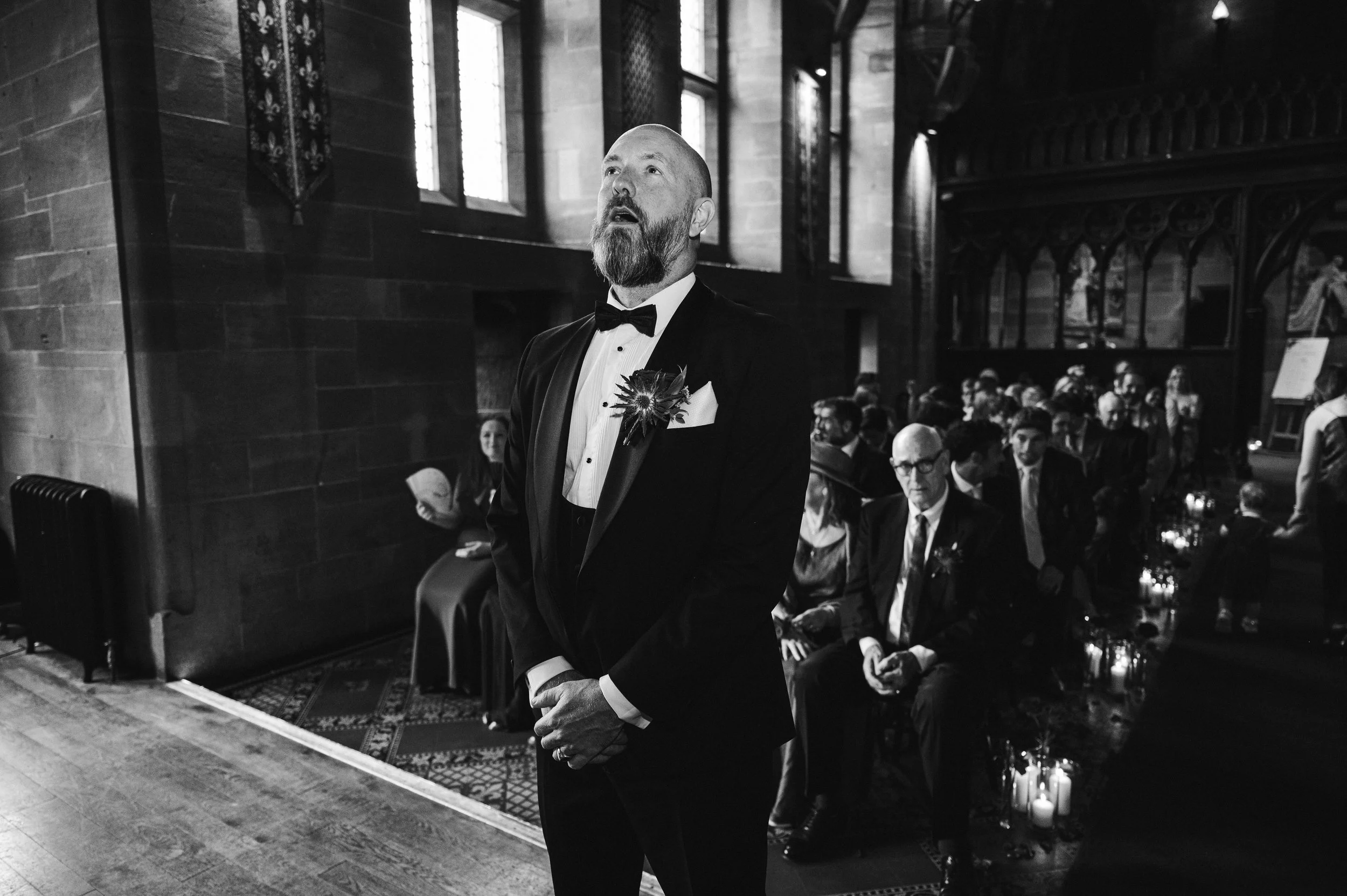 Peckforton Castle - black and white image of groom stood at the top of the aisle waiting for the bride. 