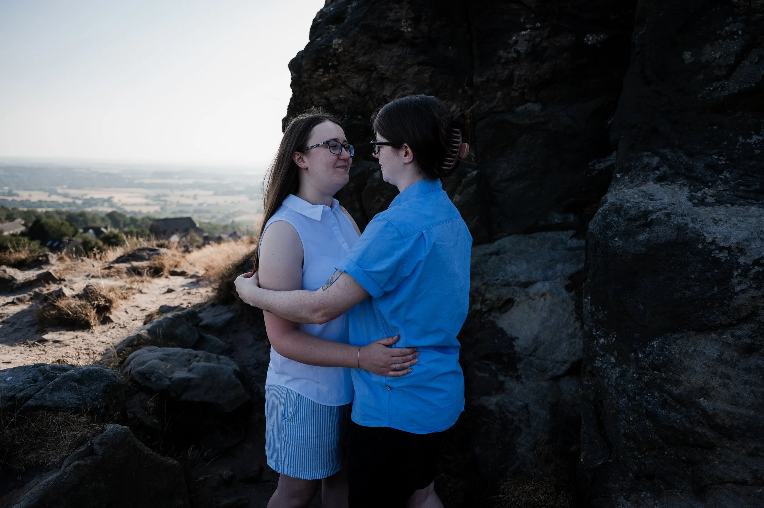 Mow Cop Engagement Shoot - two women stood in front of a landscape of Cheshire while embracing and smiling at each other