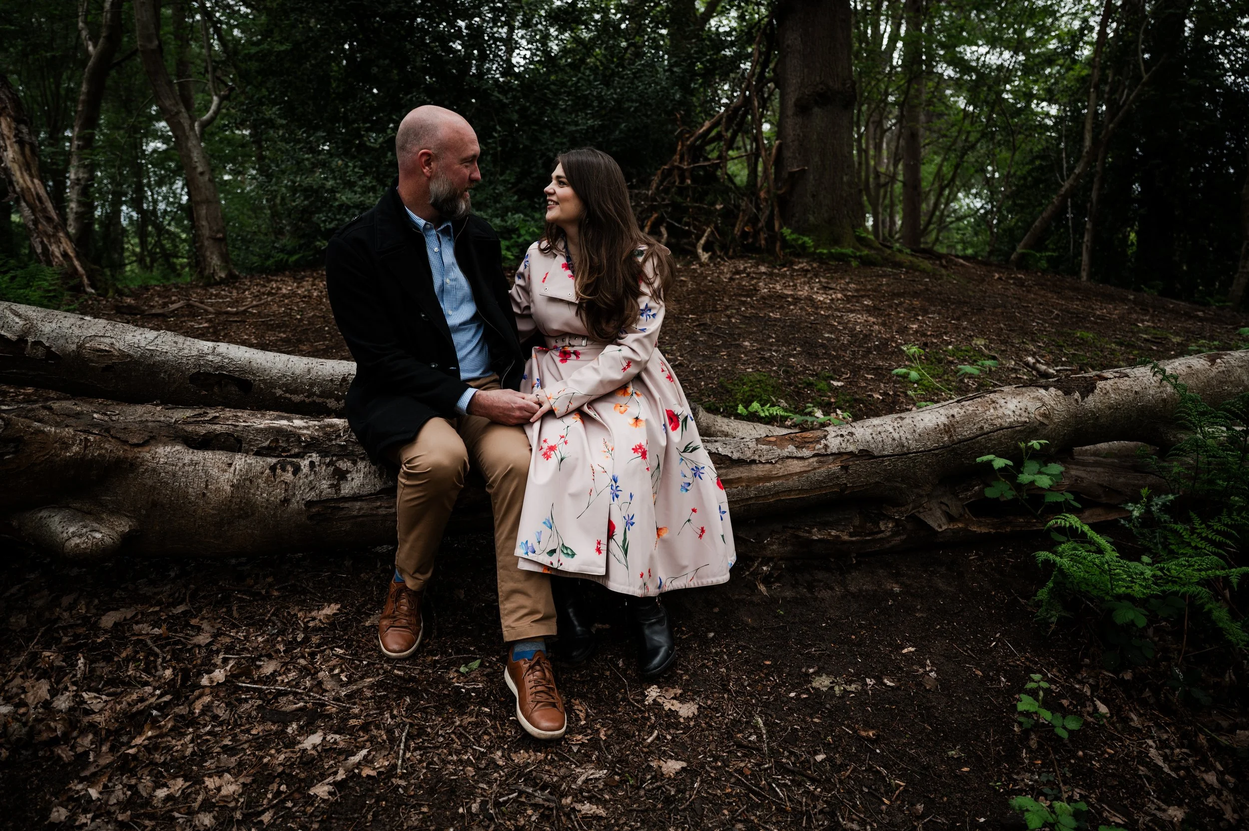 Delamere Forest Engagement shoot - man and woman sitting on a fallen tree, surrounded by greenery and woodland