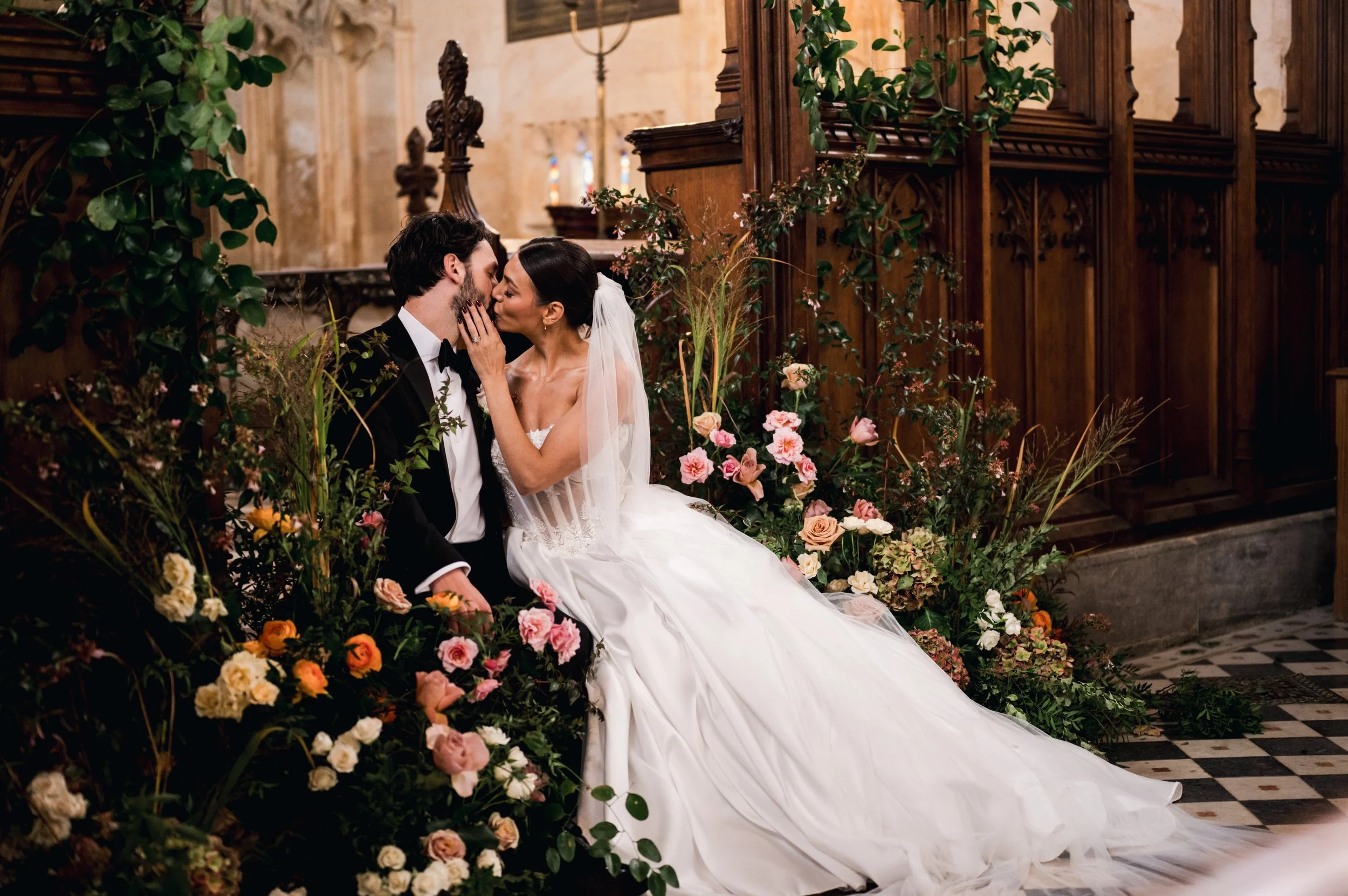 A bride and groom sharing a kiss in a church surrounded by floral arrangements at sudeley castle, Gareth roy photography