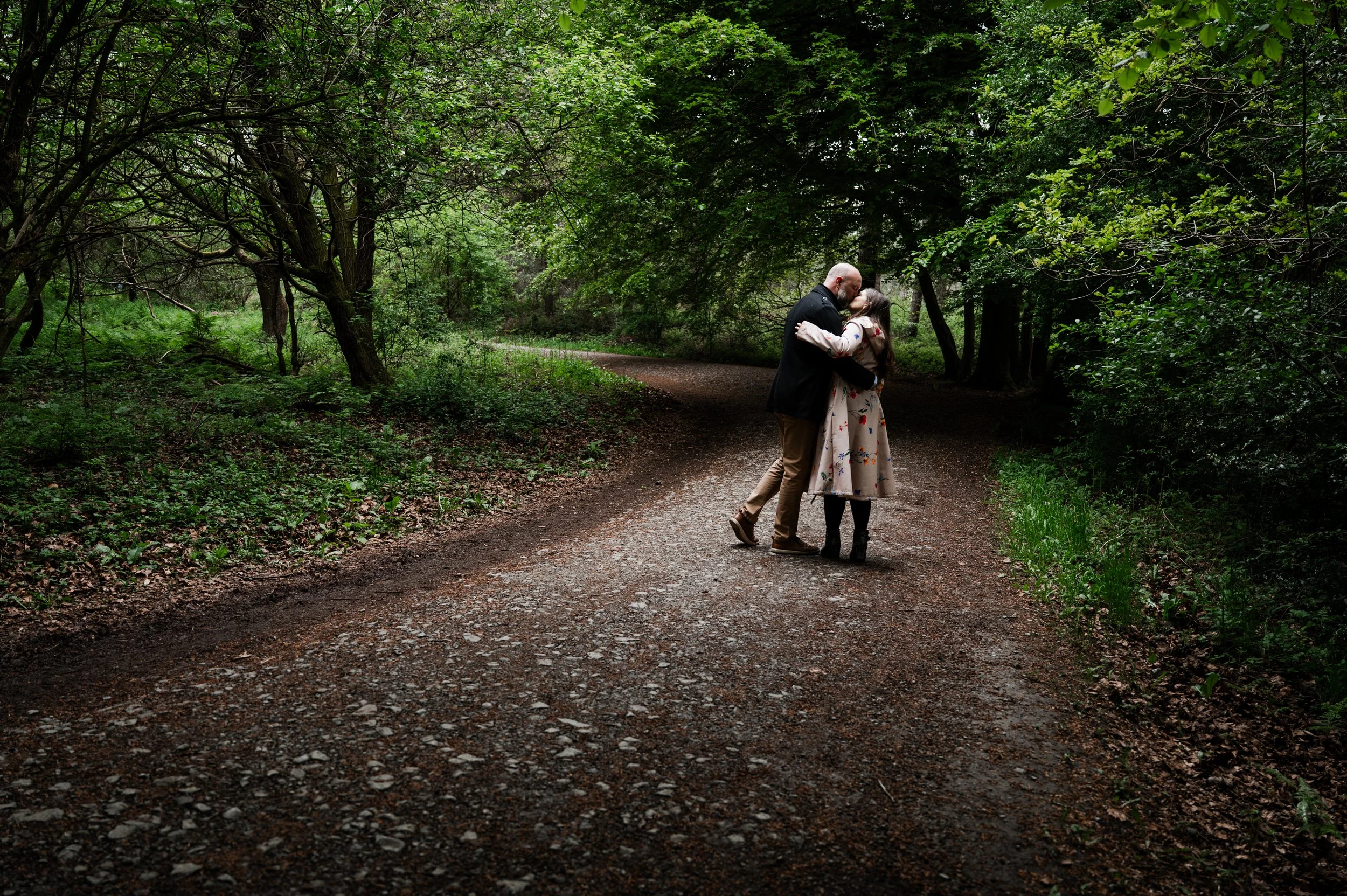 Delamere Forest Engagement shoot - man and woman embraced and kissing with woodland behind them while walking away from the camera