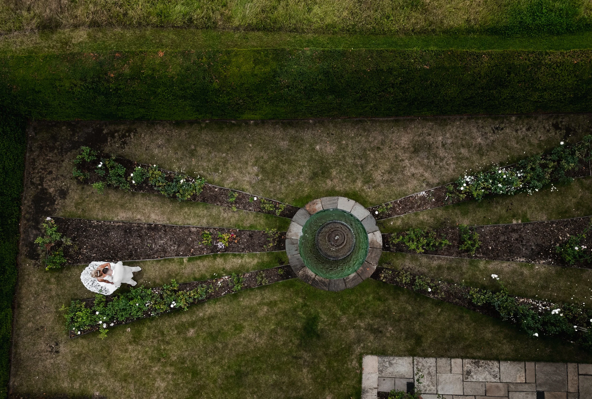 The Love Shack - Drone image of groom and bride in wedding attire, walking through gardens