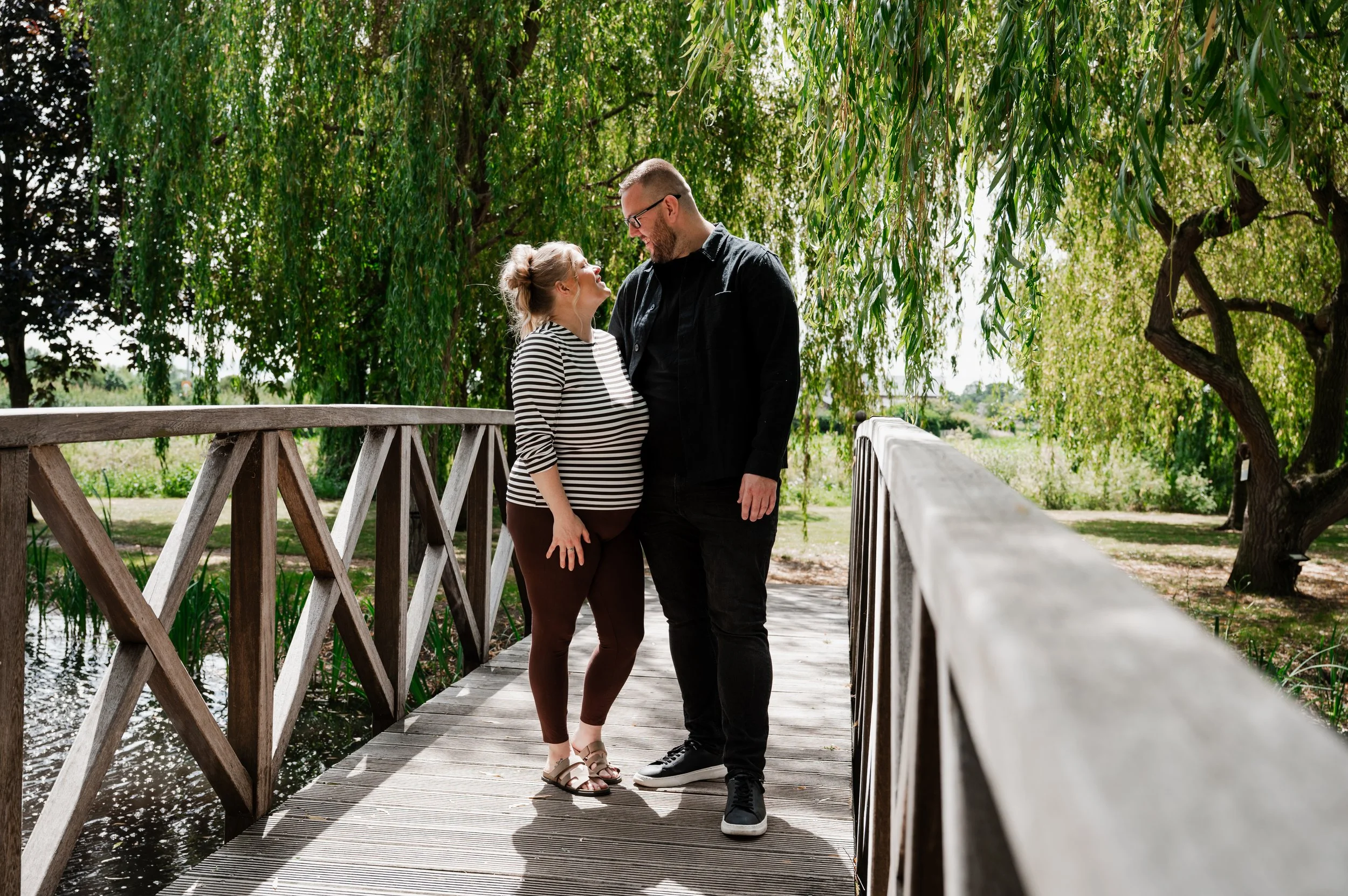 The Grosvenor Pulford Engagement - man in black shirt and woman in striped top, smiling at each other while walking over a wooden bridge
