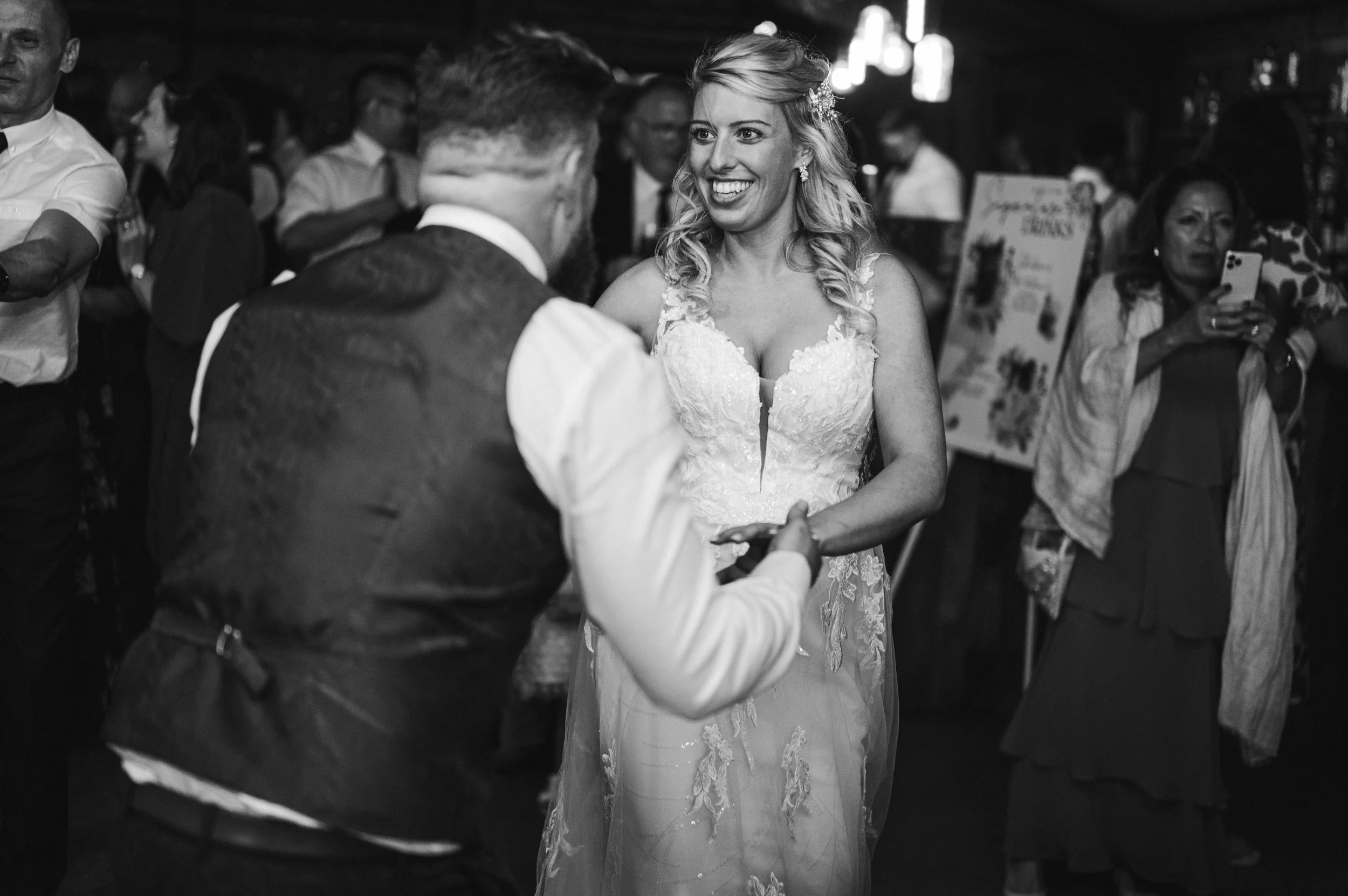 A bride and groom dancing at their wedding reception, smiling and holding hands, with guests in the background grange barn Whitchurch, Gareth roy photography