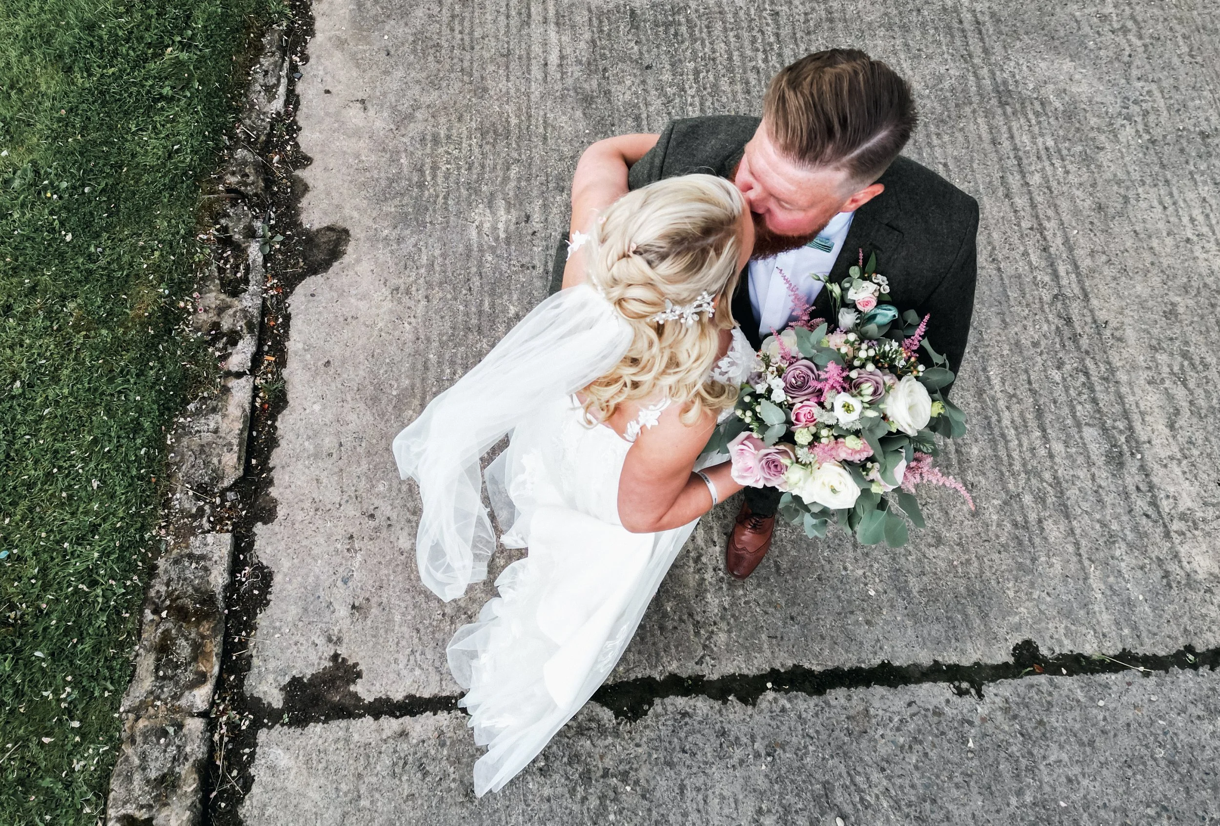 Overhead view of a bride and groom sharing a kiss on a concrete sidewalk, with the bride holding a floral bouquet grange barn Whitchurch, Gareth roy photography