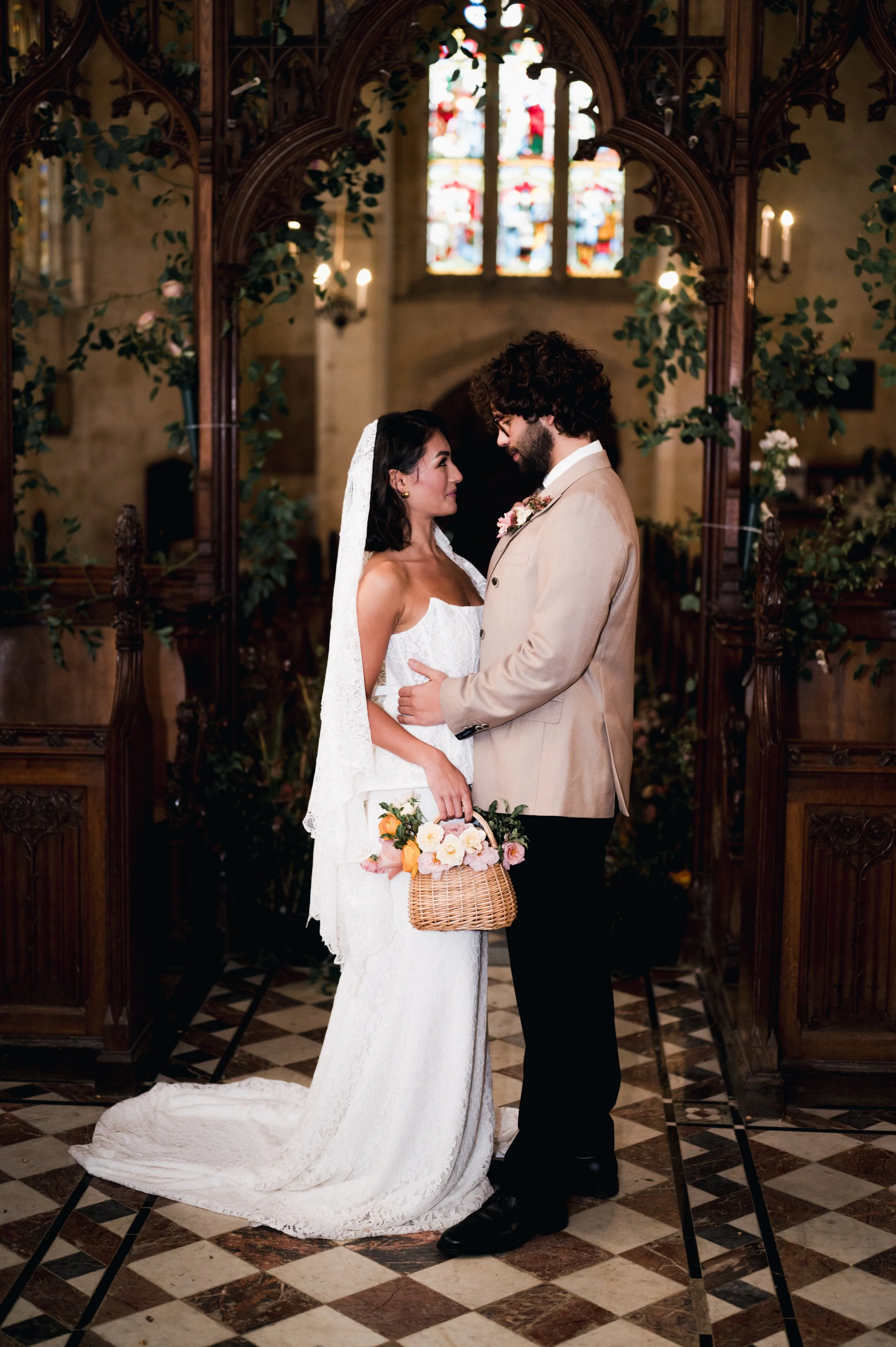 Couple in wedding attire sharing a moment in a church with stained glass windows and gothic architecture at sudeley castle