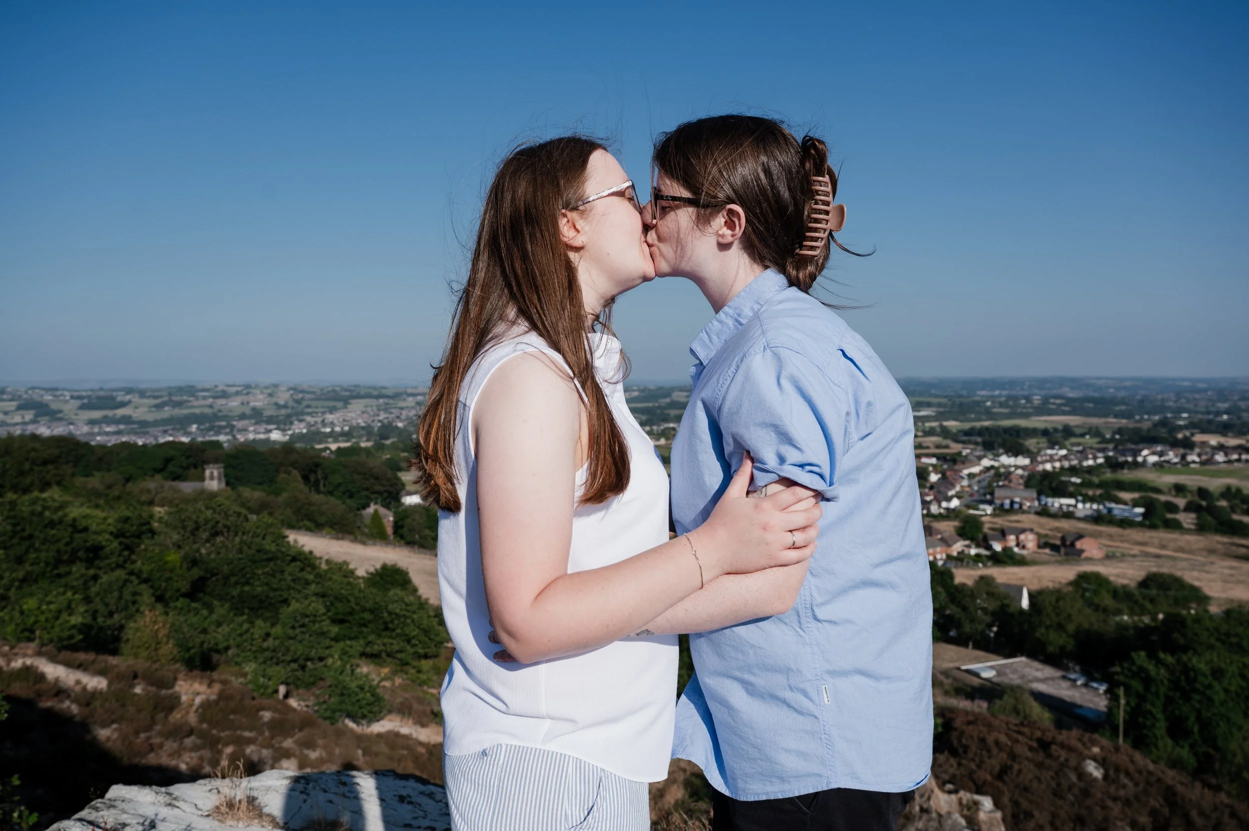 Mow Cop Engagement Shoot - two women stood in front of a landscape of Cheshire while embracing and kissing