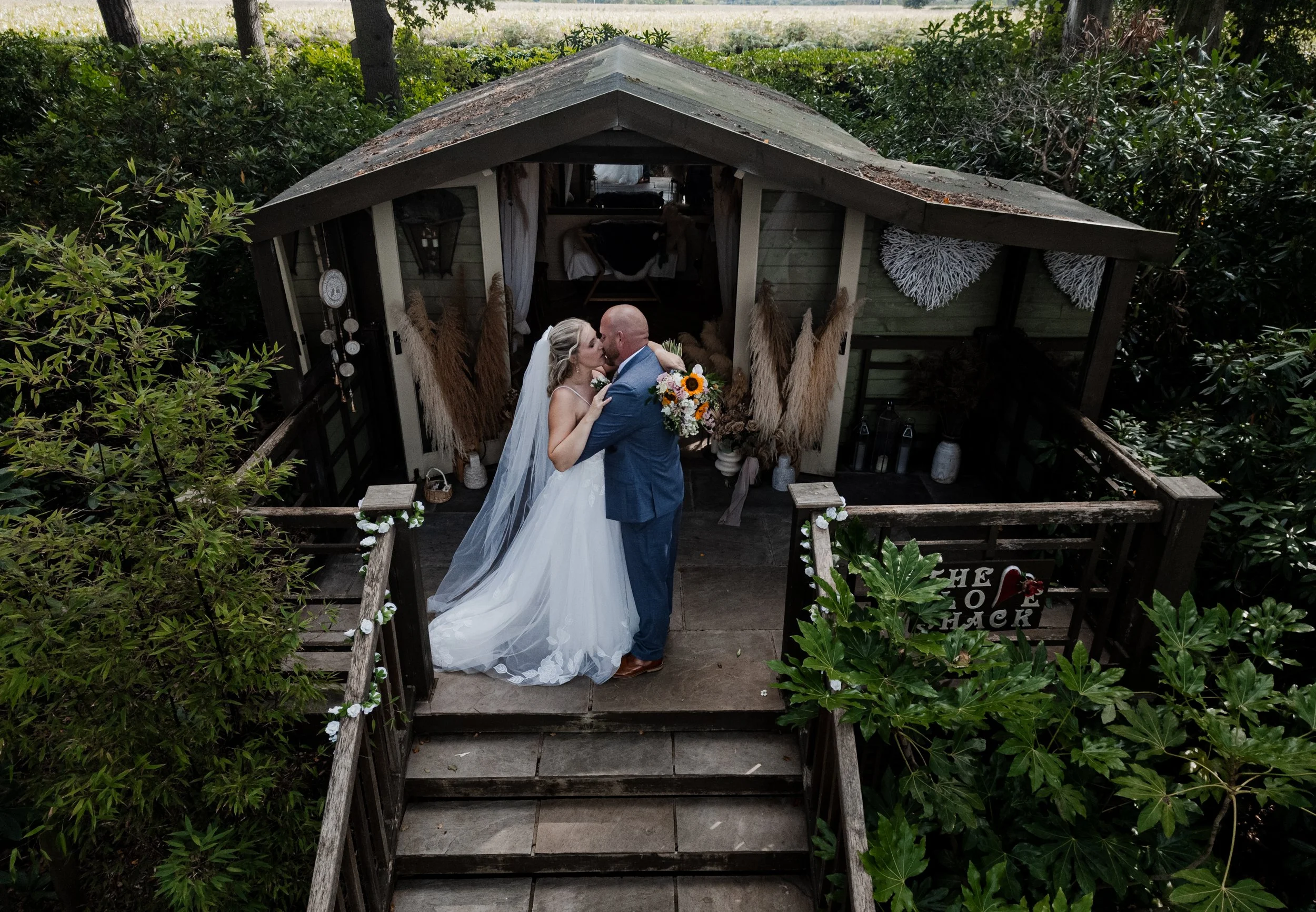 Wedding Photography Cheshire - Bride and groom in wedding attire, kissing in front of a wooden wedding venue on top of stairs. 